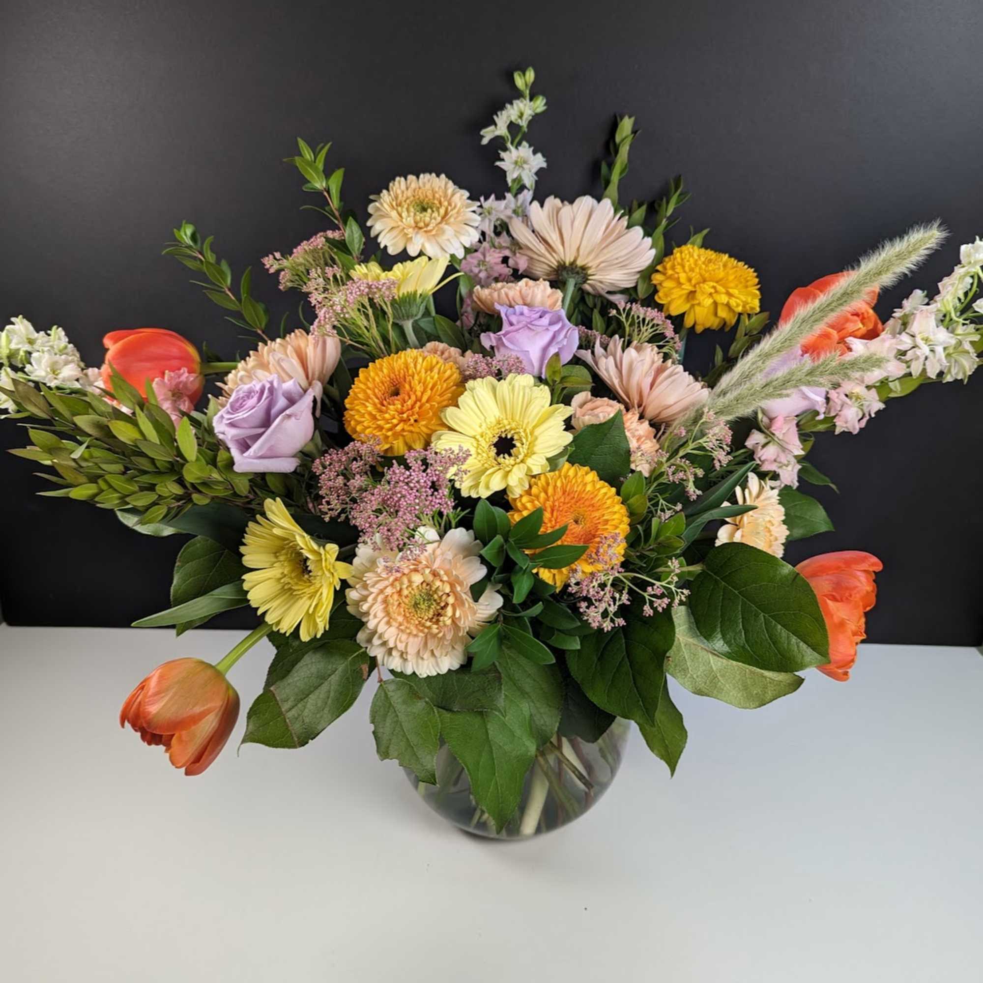 Mixed bouquet in a glass vase with orange tulips and pastel daisies
