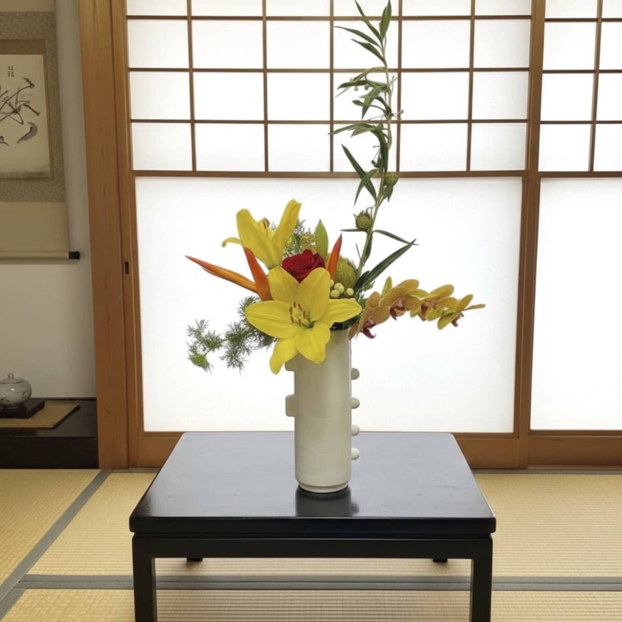 Tall floral arrangement with yellow lilies and orchids in a white vase