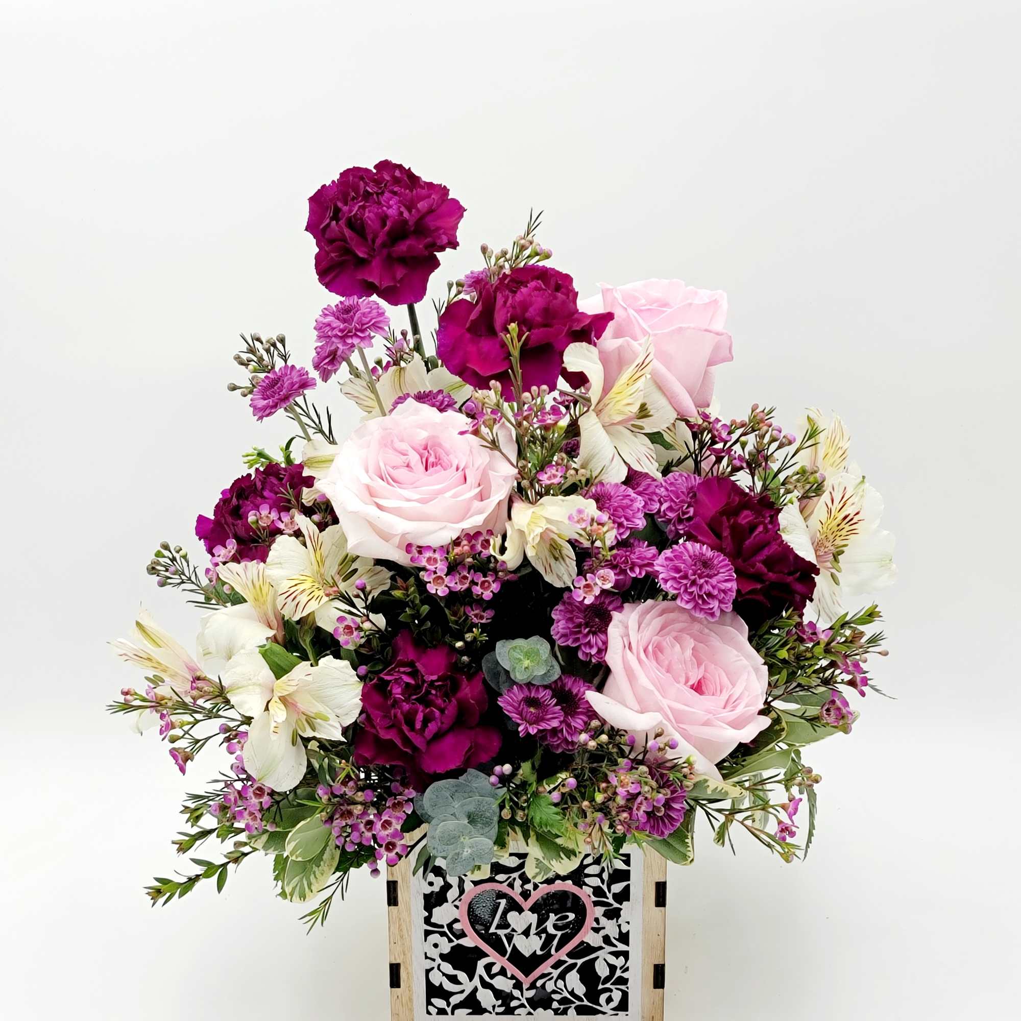 Pink and purple floral arrangement in a wooden box with a heart sign