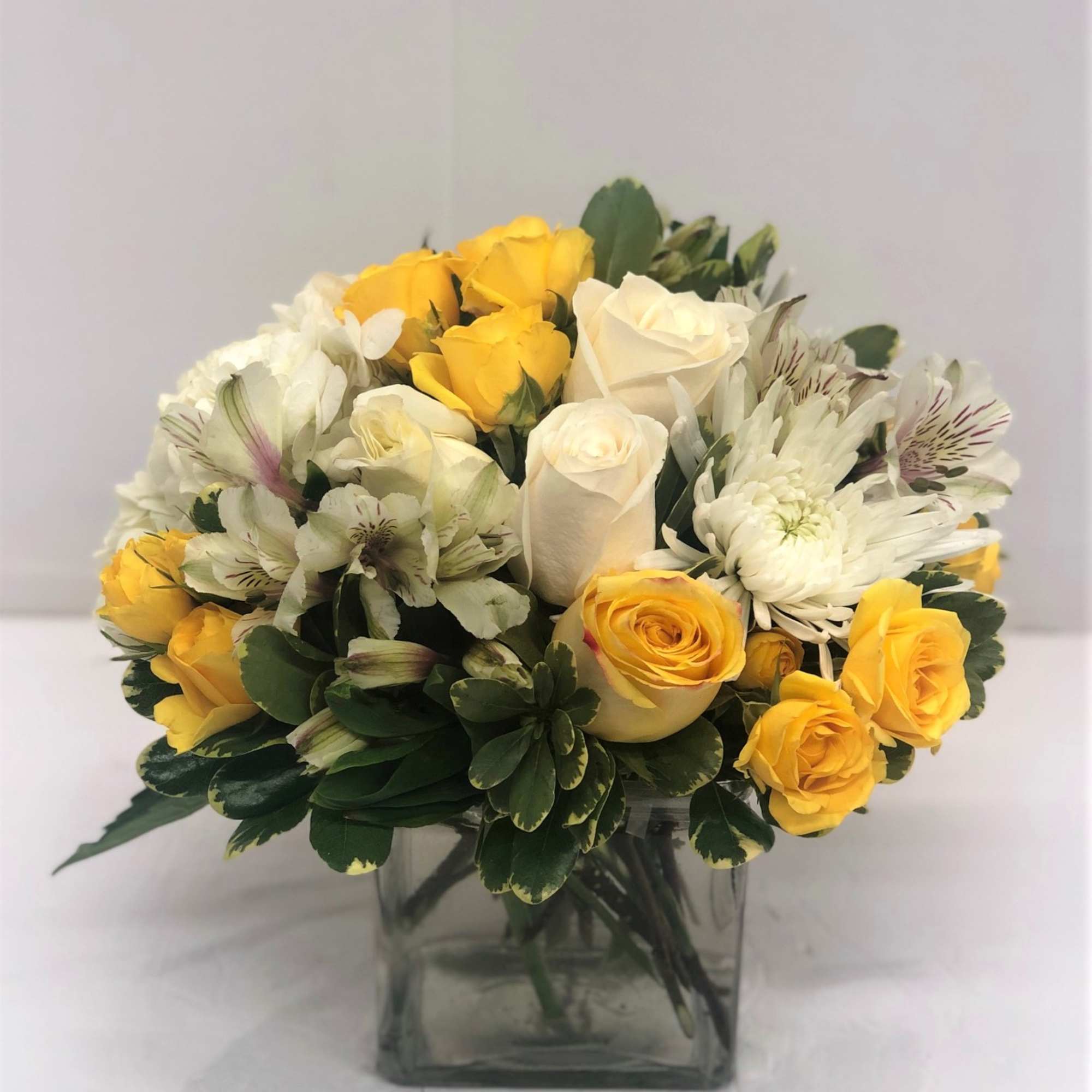 Yellow and white roses arranged in a square glass vase