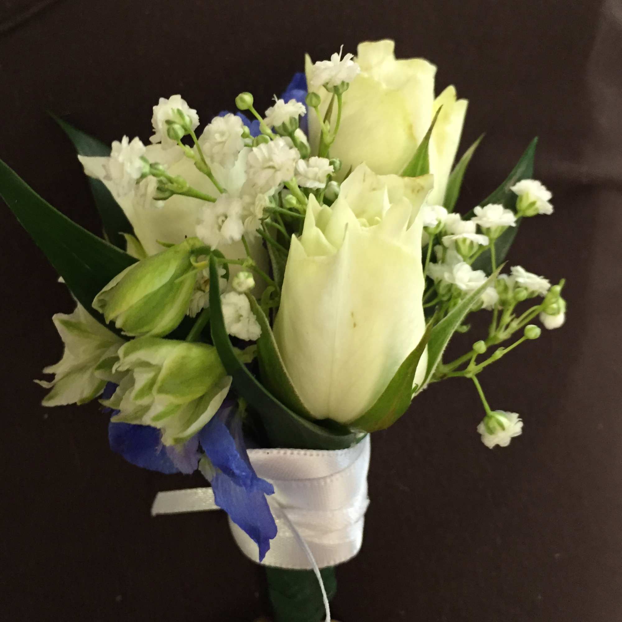 White tulips and small white flowers with blue accents in a wrapped bouquet