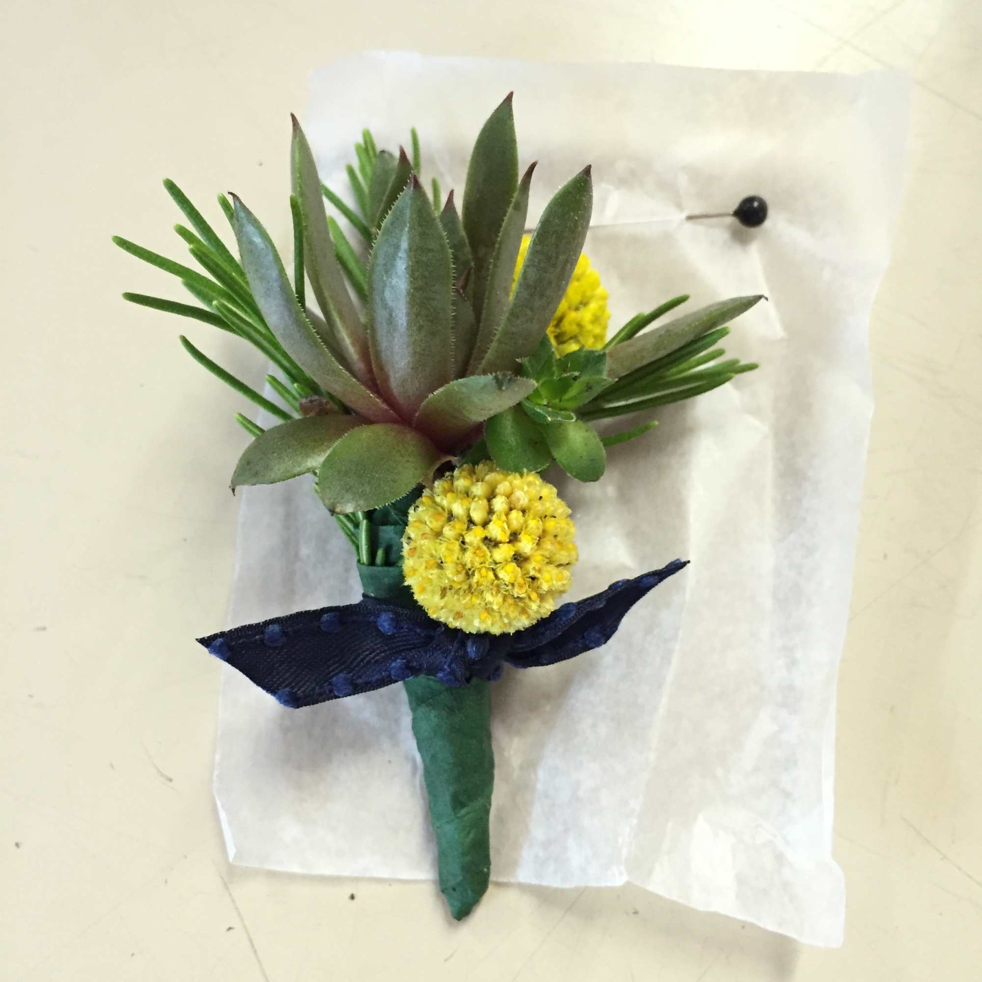 Boutonniere with a succulent, yellow pom-pom flowers, and a navy ribbon