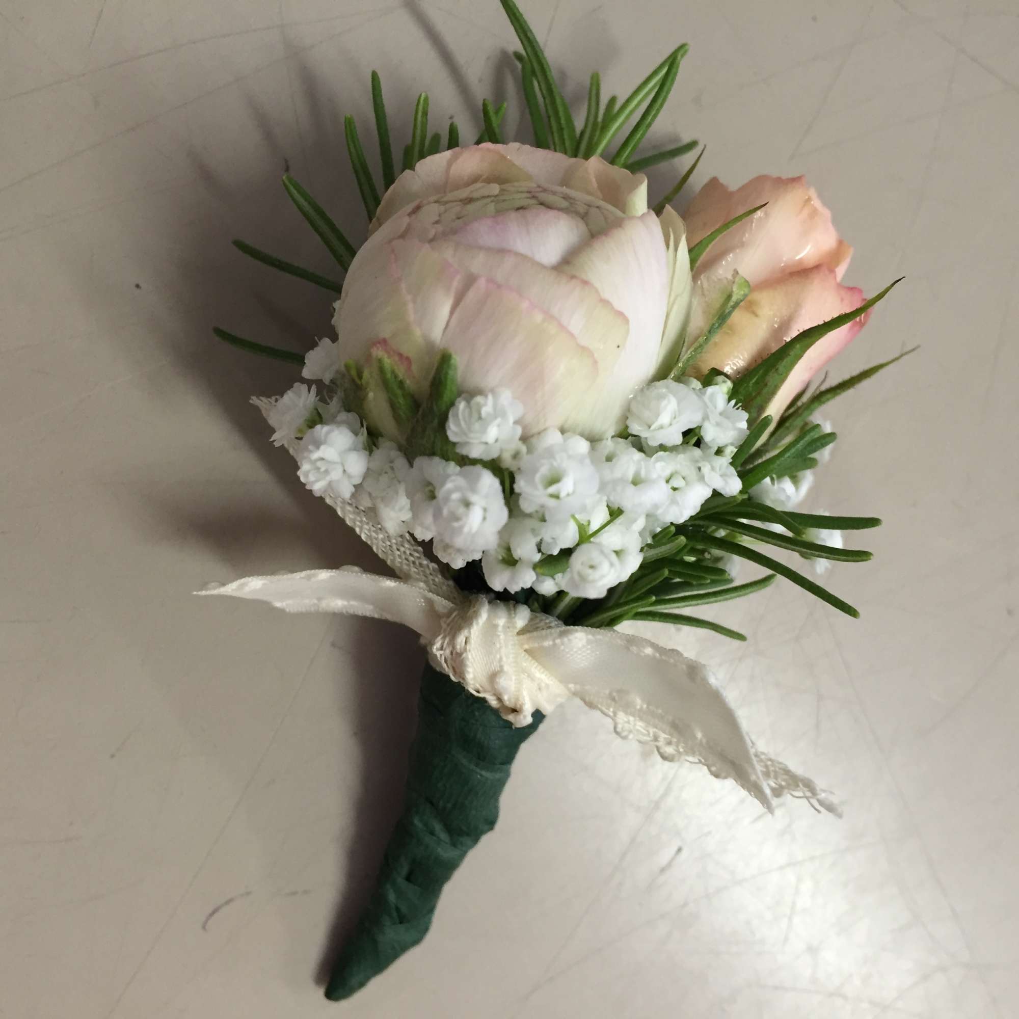 Small boutonniere with pale pink roses, white filler flowers, and a cream ribbon.