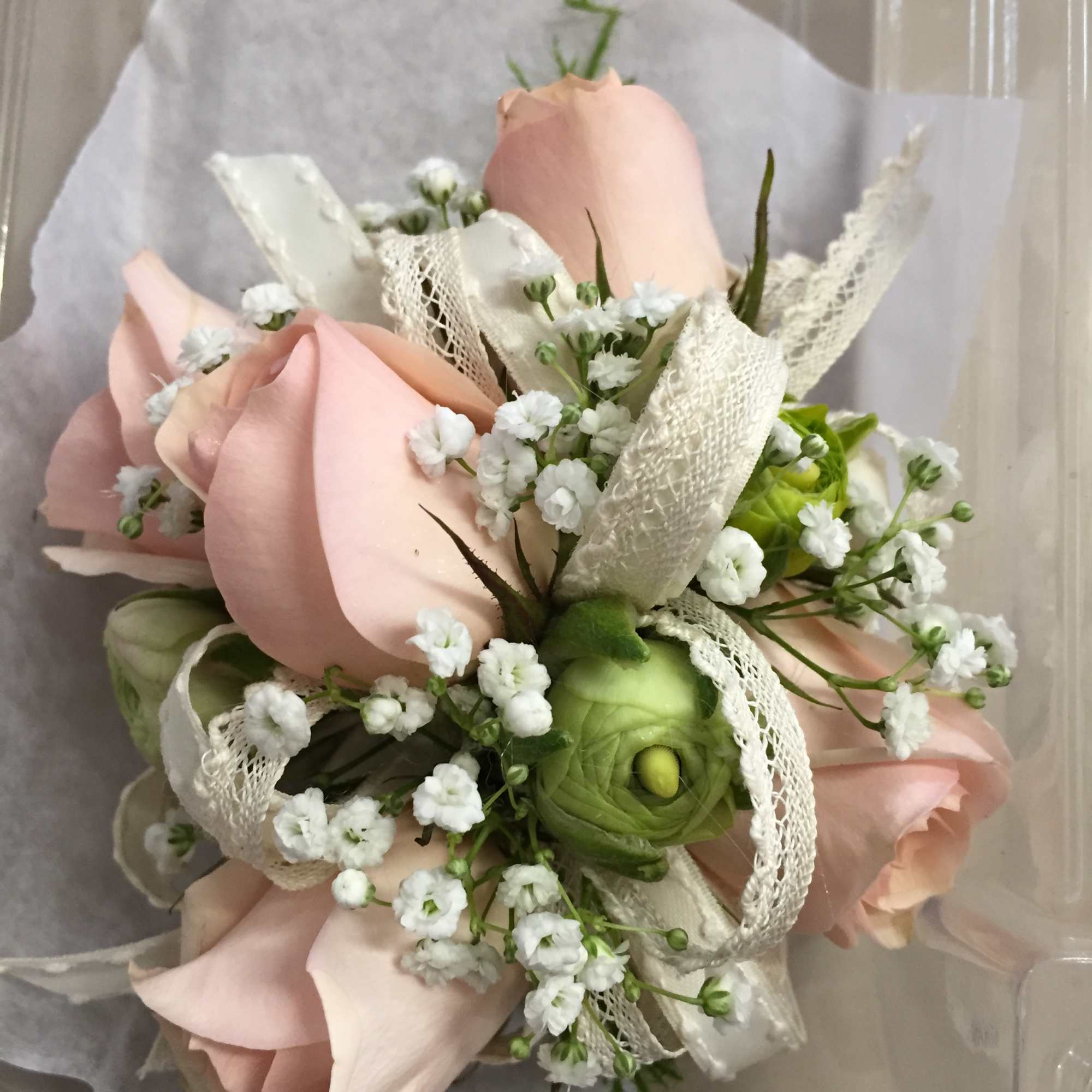Small bouquet of pale pink roses with white filler flowers and lace ribbon.
