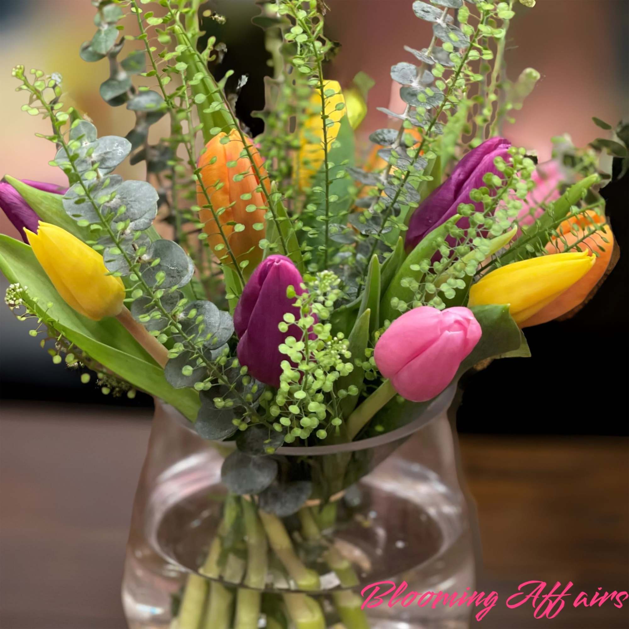 Colorful tulips in a clear glass vase with eucalyptus