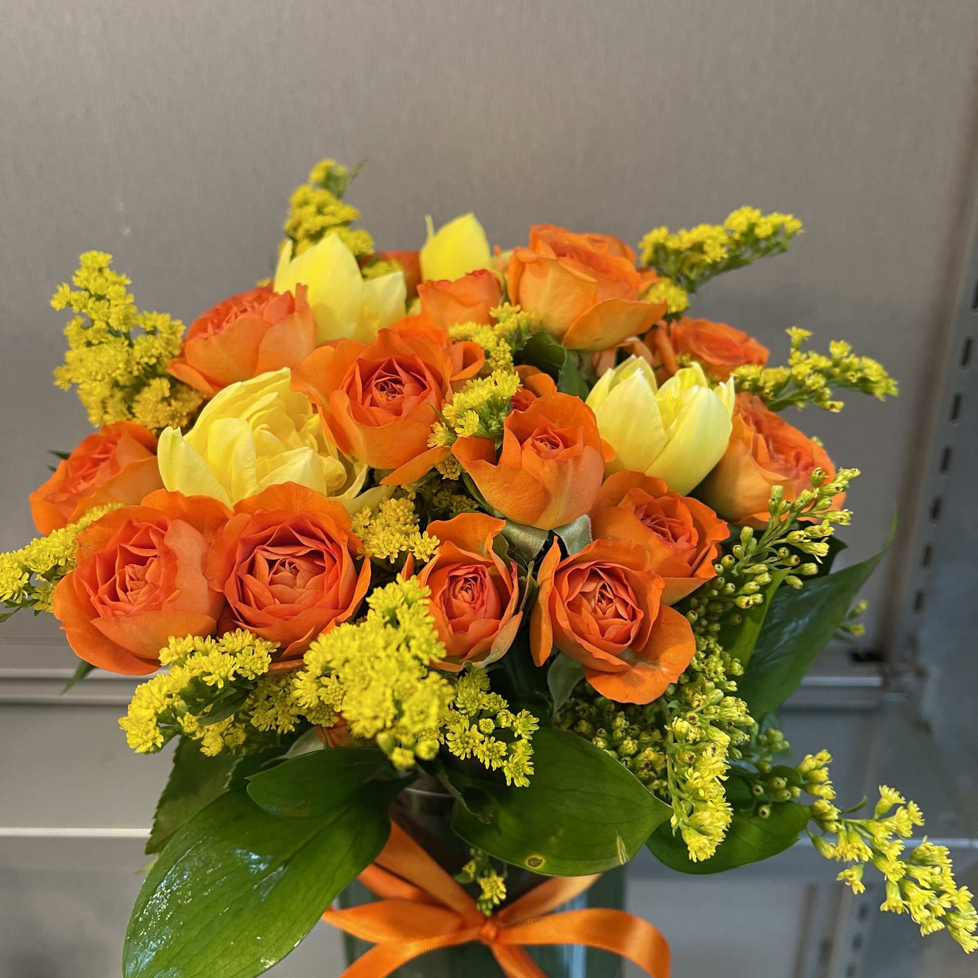 Orange and yellow rose bouquet in a glass vase with an orange ribbon