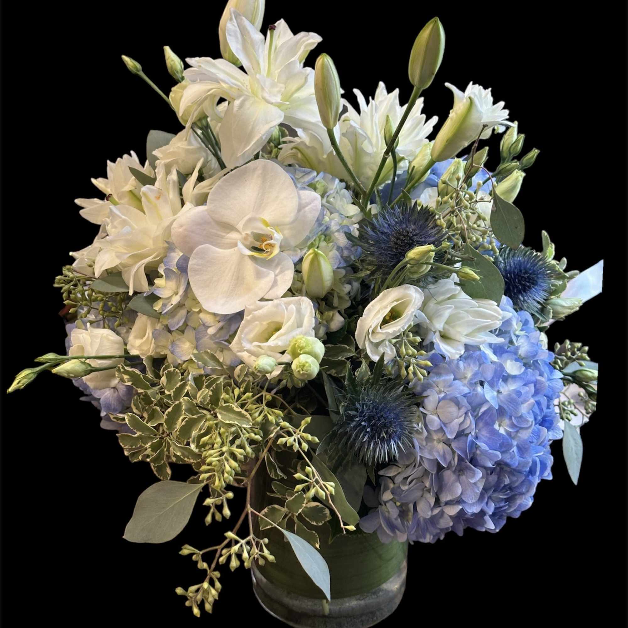 White lilies, orchids, and blue hydrangeas in a glass vase