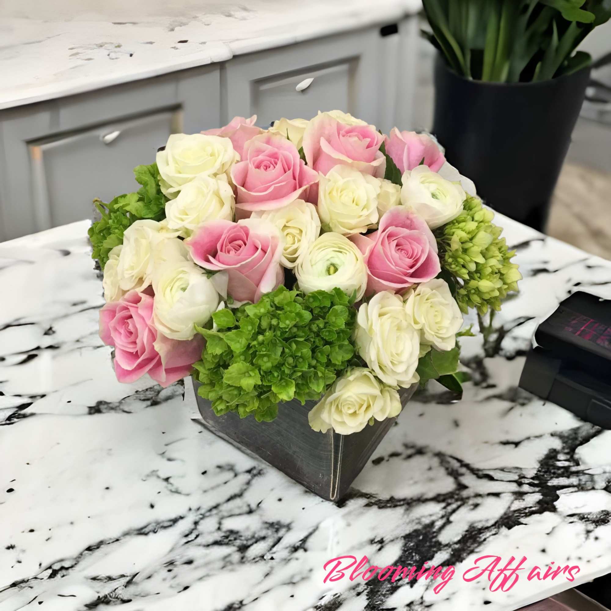Pink and white roses arranged in a low black box with green hydrangeas
