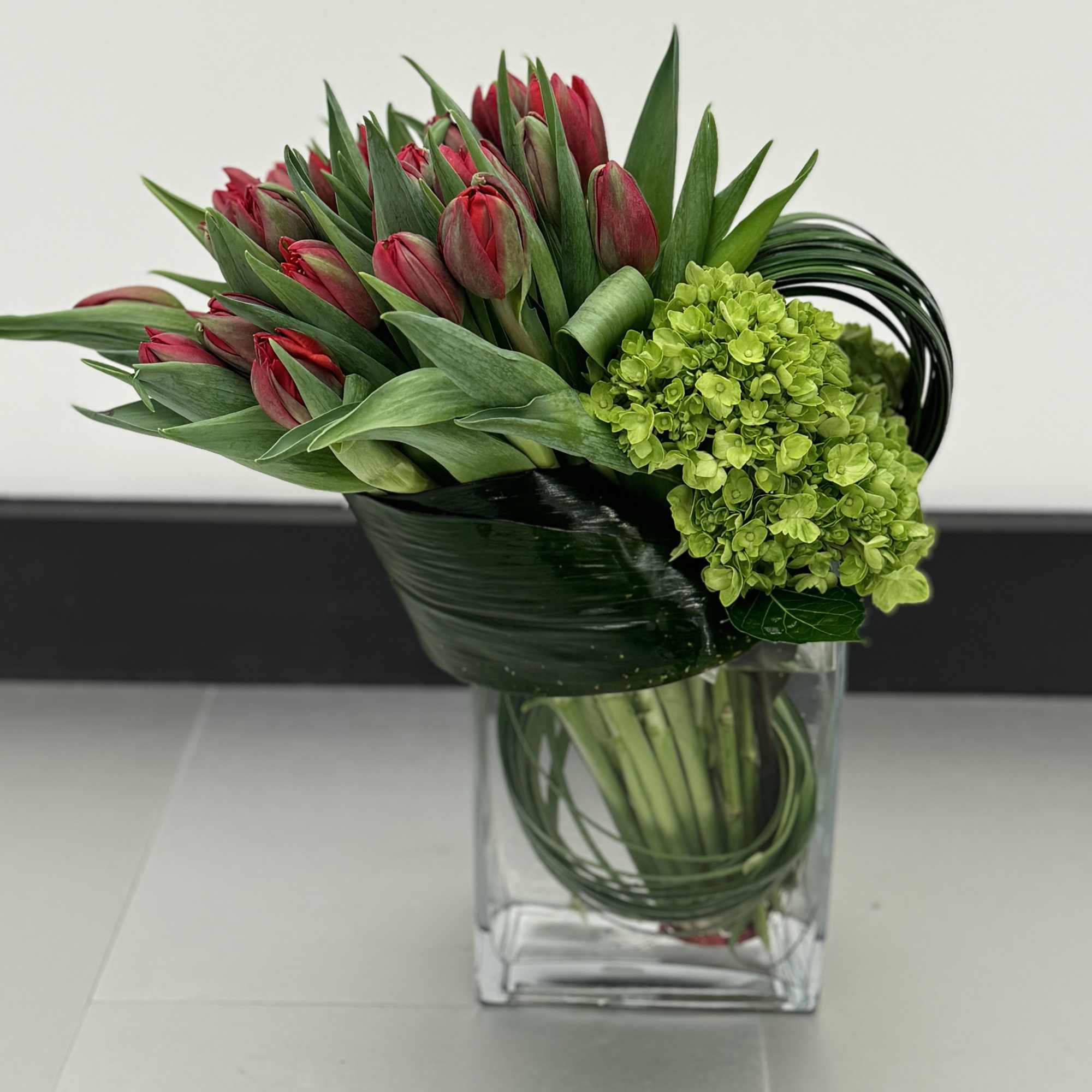 Red tulips and green hydrangea in a clear glass vase