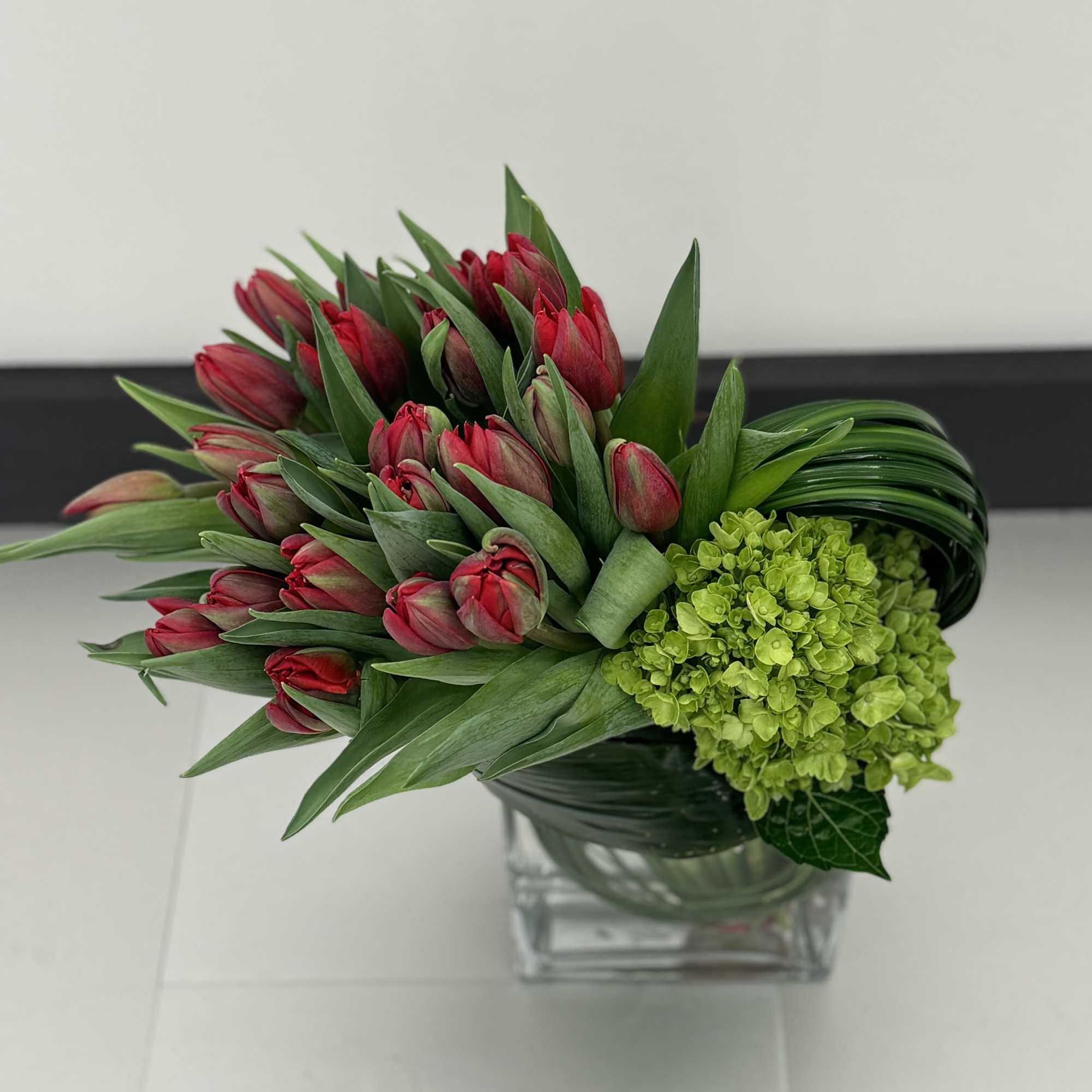 Bouquet of red tulips and green hydrangea in a glass vase