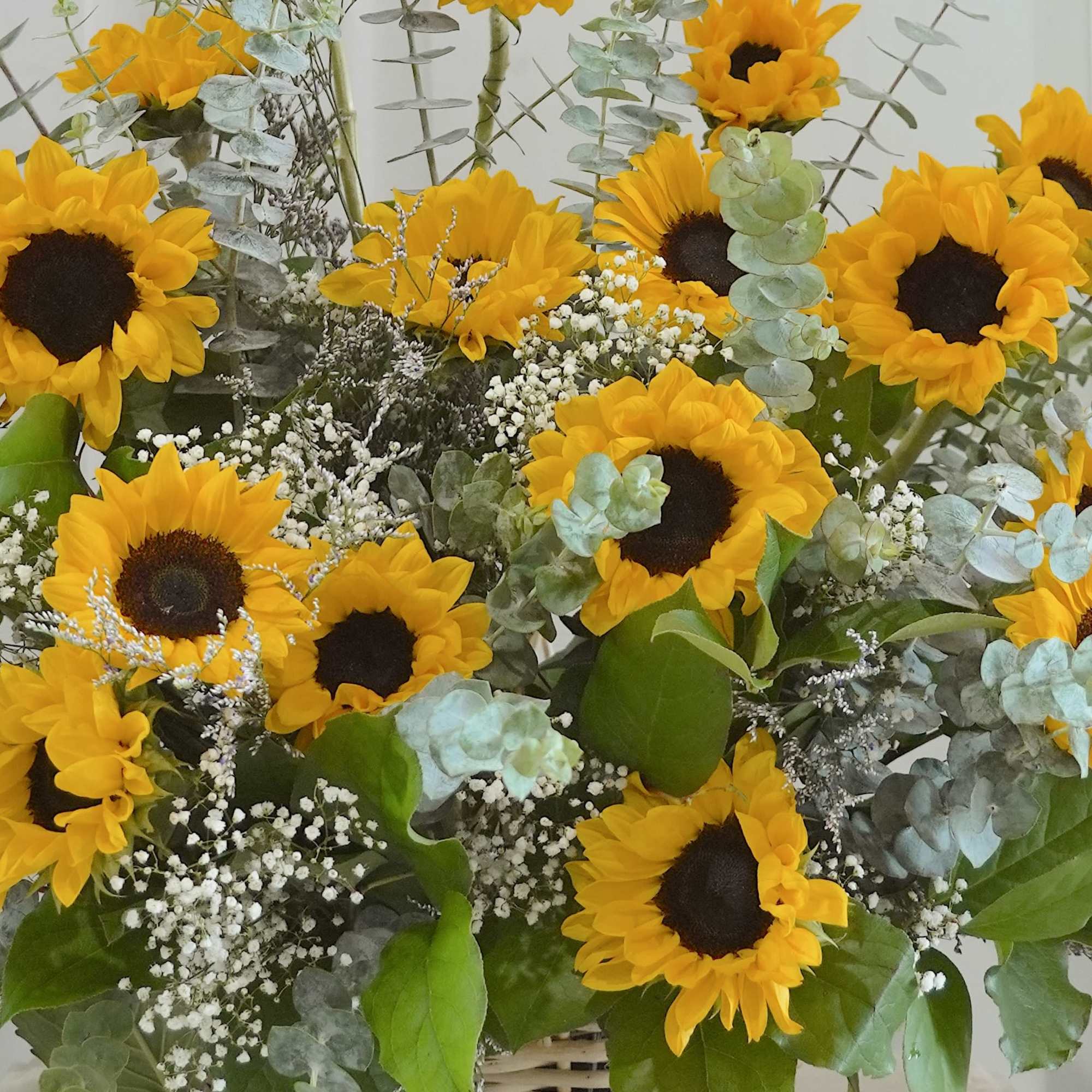Bright yellow sunflowers with white fillers and silvery-green eucalyptus in a woven