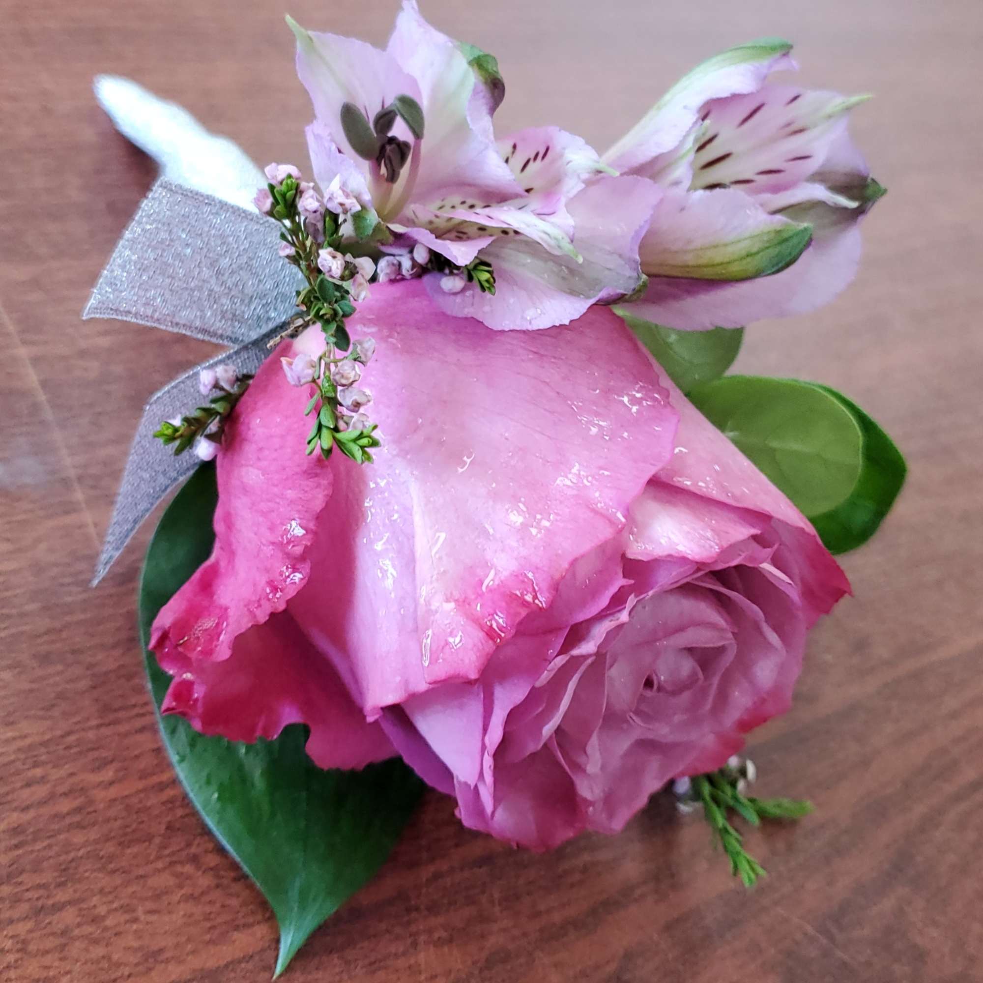 Pink rose boutonniere with small white flowers and silver ribbon