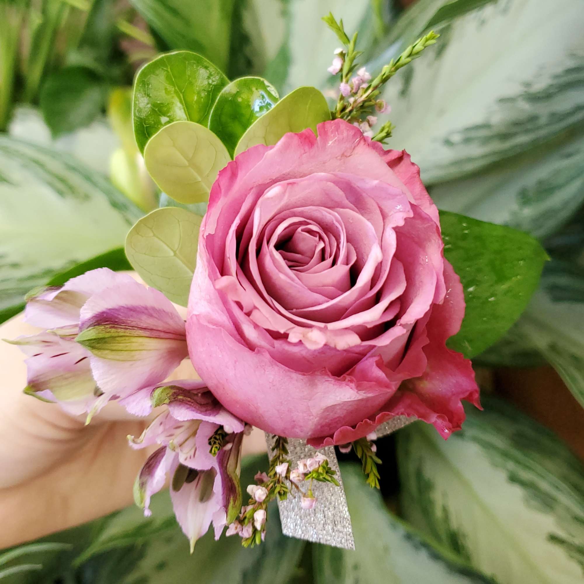 Pink rose boutonniere with small purple flowers and green leaves