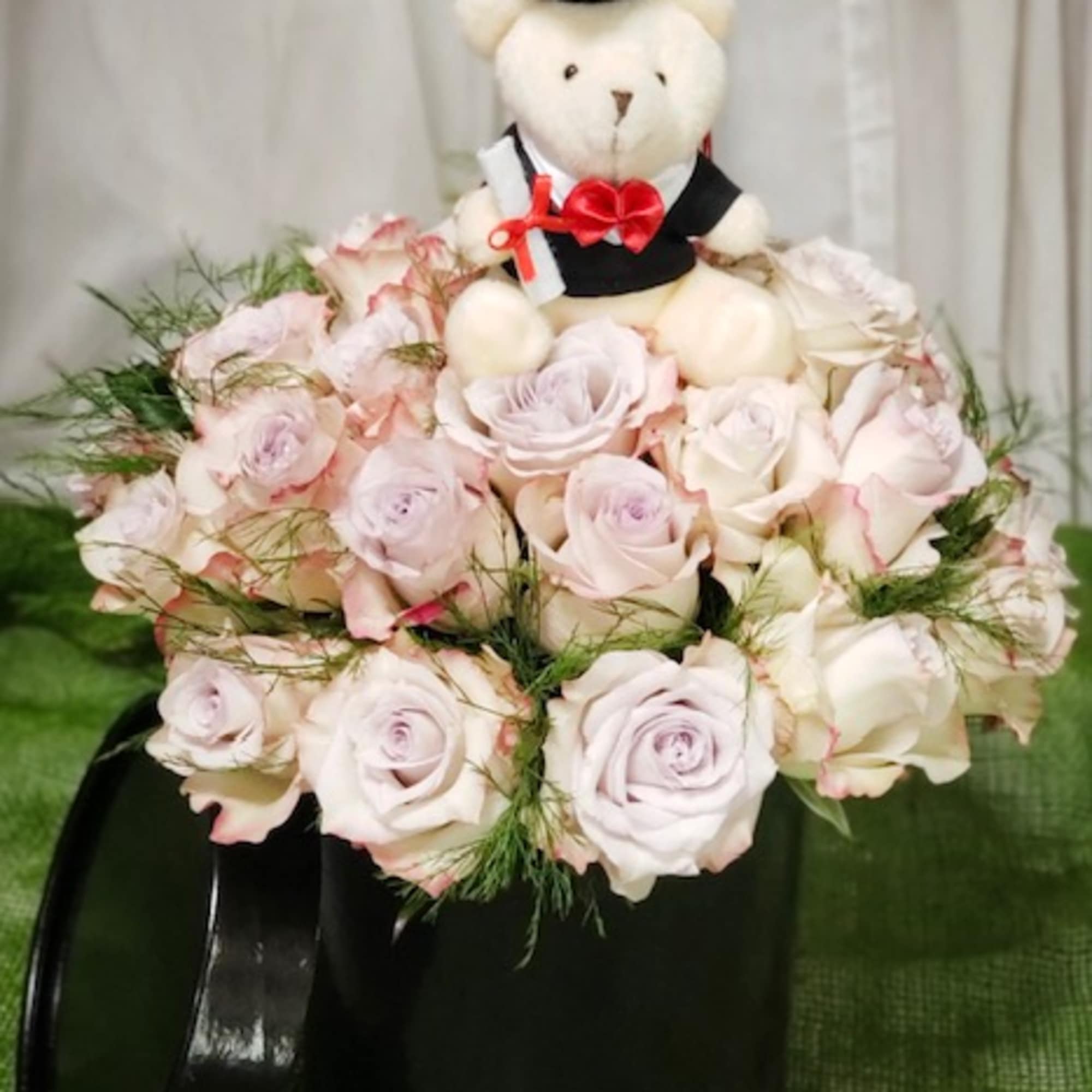 Teddy bear in a graduation cap sitting in a bouquet of pale pink roses