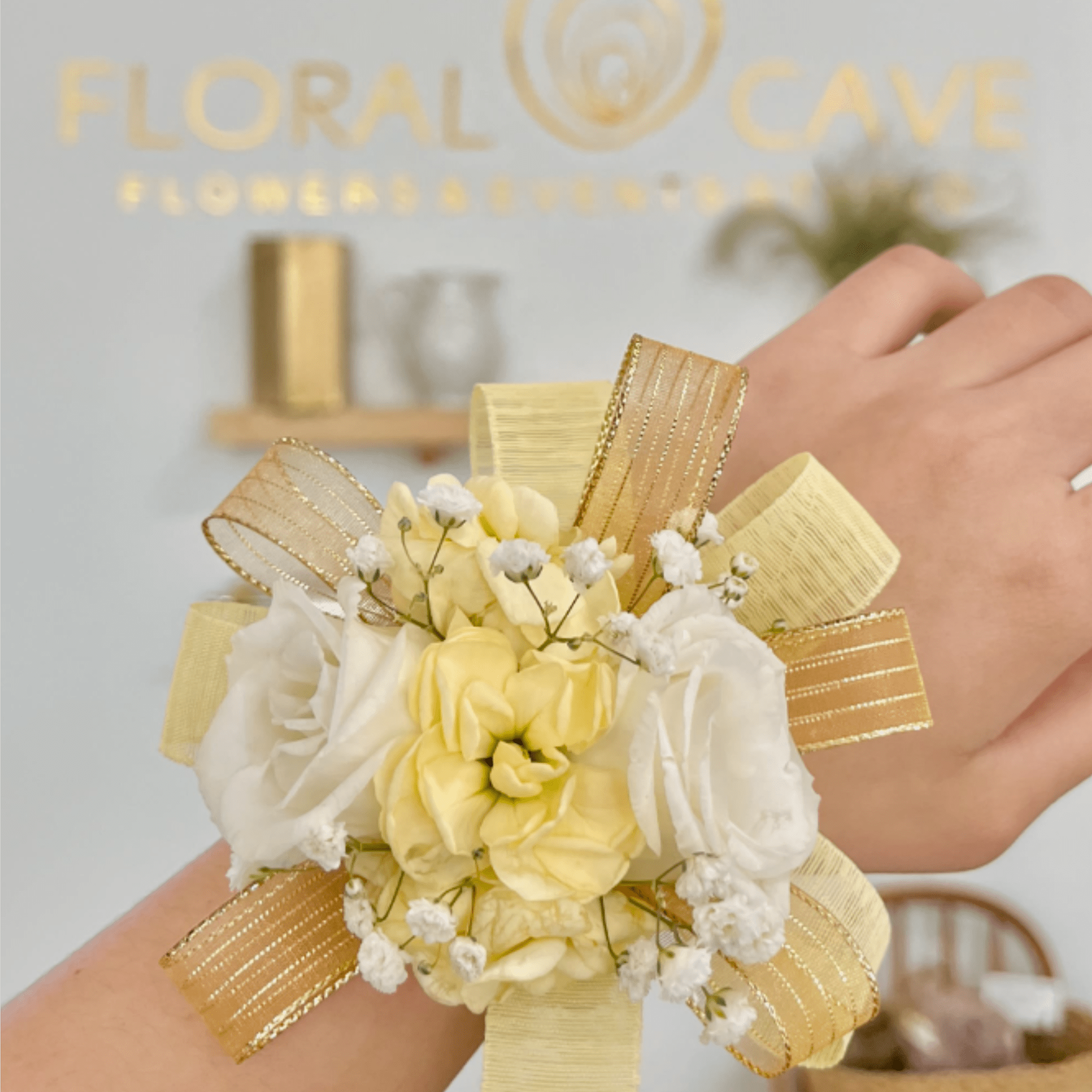 Yellow and white wrist corsage with small flowers and gold ribbon on a person’s arm