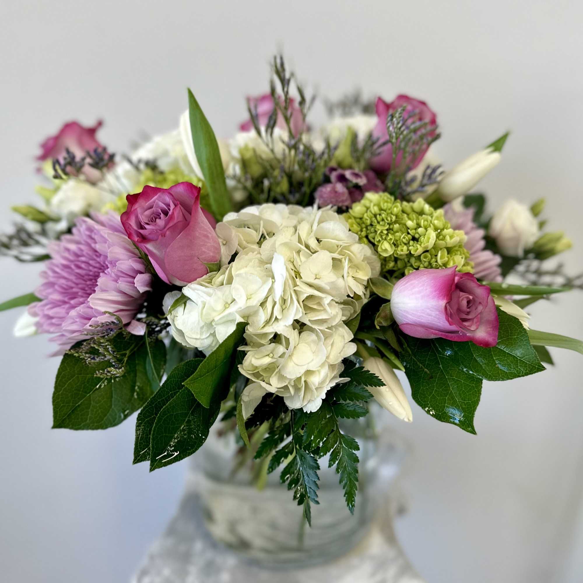 Bouquet of pink roses, white hydrangea, and lavender blooms in a glass vase