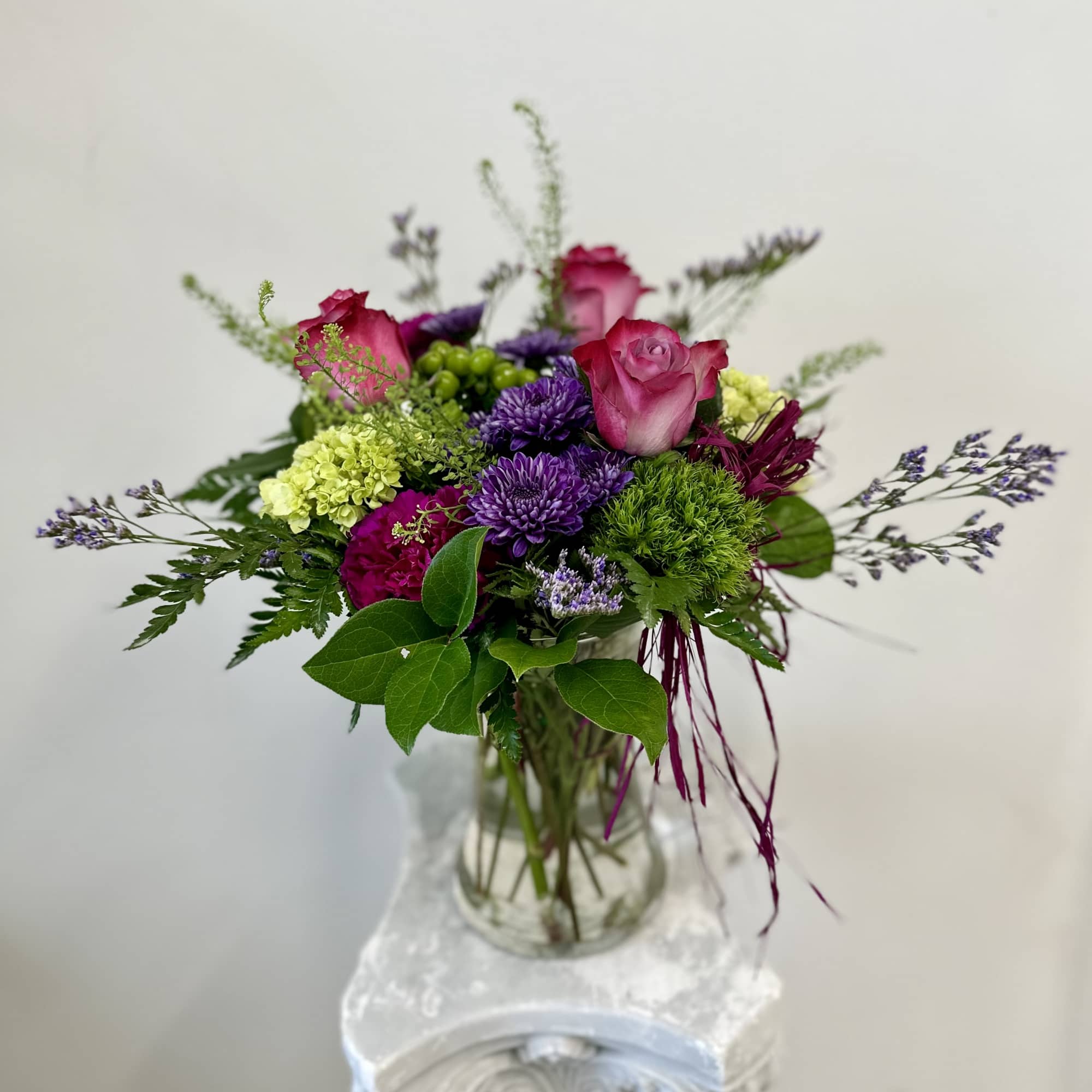 Mixed bouquet of pink roses and purple flowers in a clear glass vase