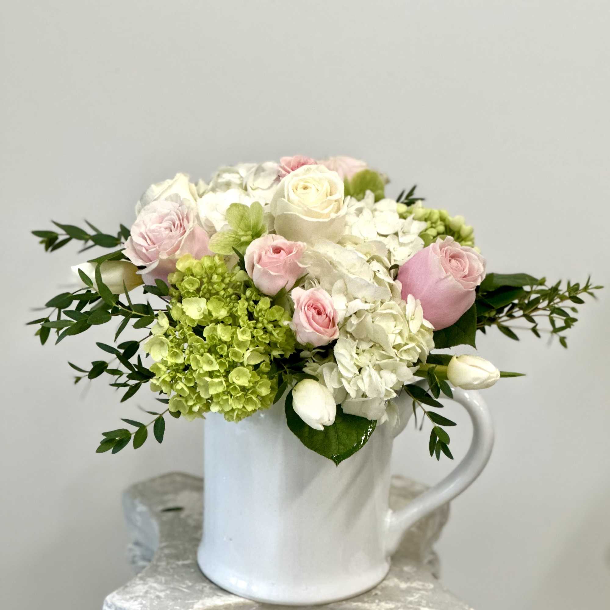 Pink and white roses with hydrangeas in a white mug vase