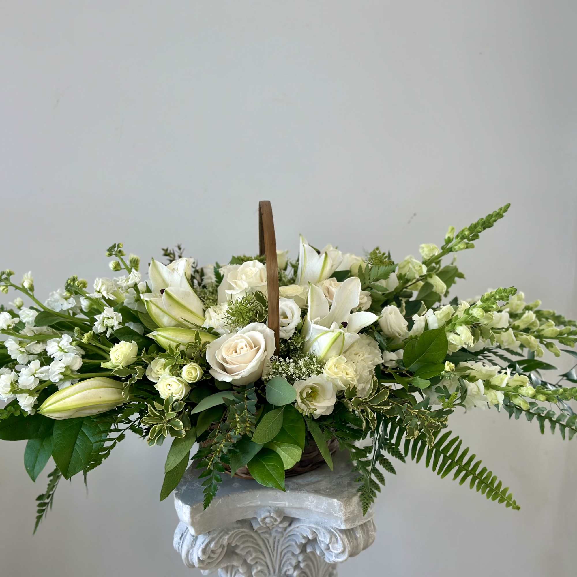 White floral arrangement in a basket with lilies and roses