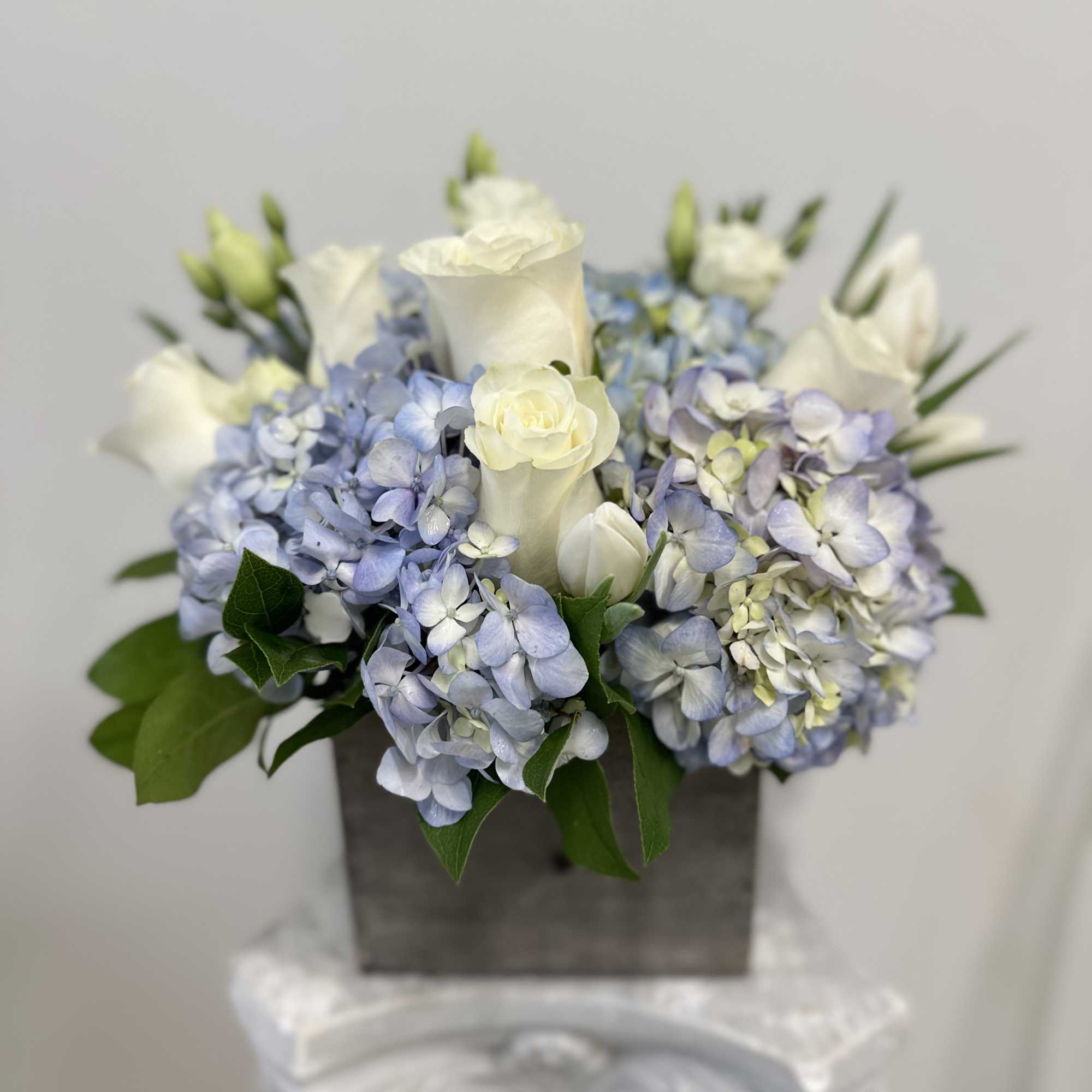 Compact arrangement of white roses and blue hydrangeas in a gray wooden box