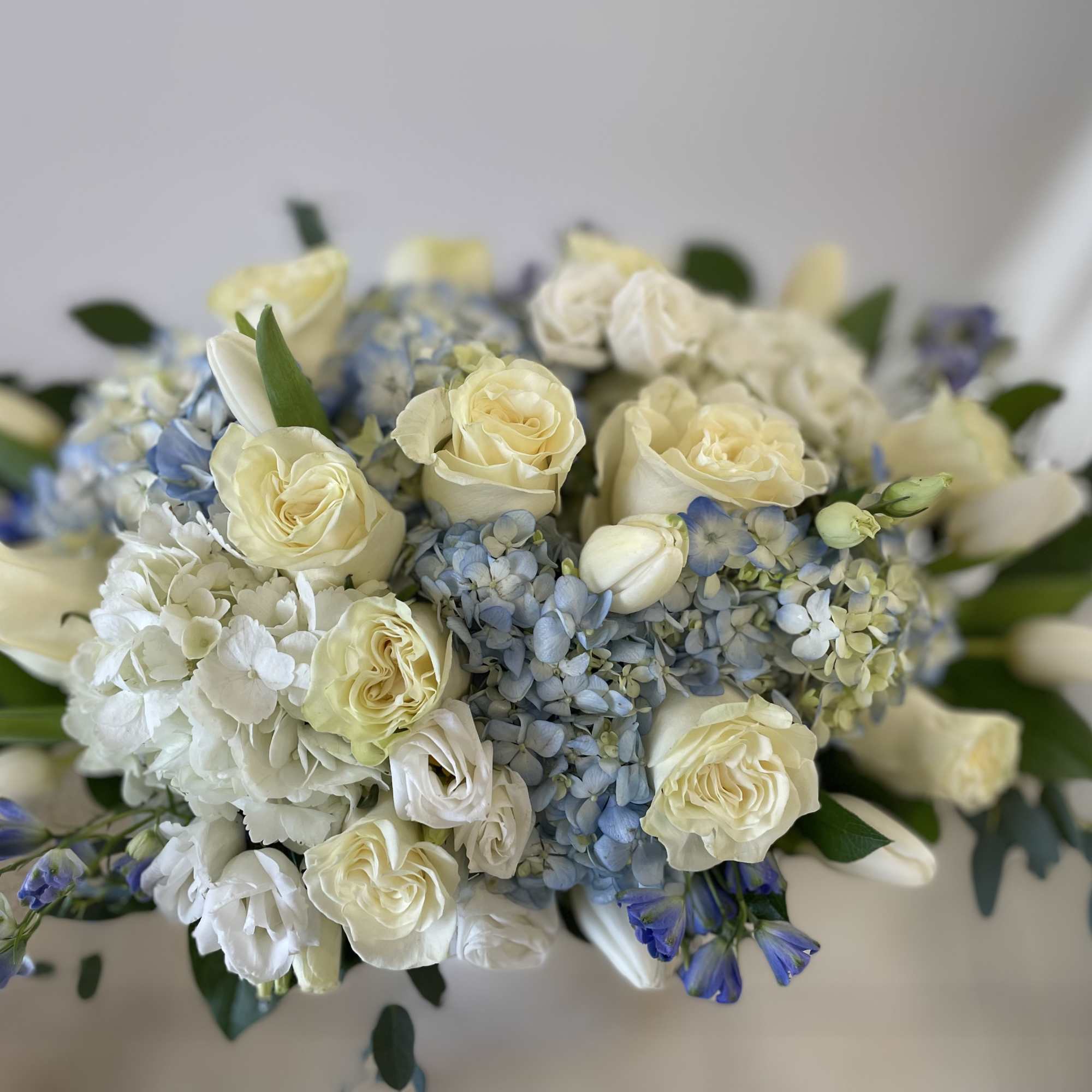 Round arrangement of ivory roses, white hydrangeas, blue hydrangeas, and white tulips