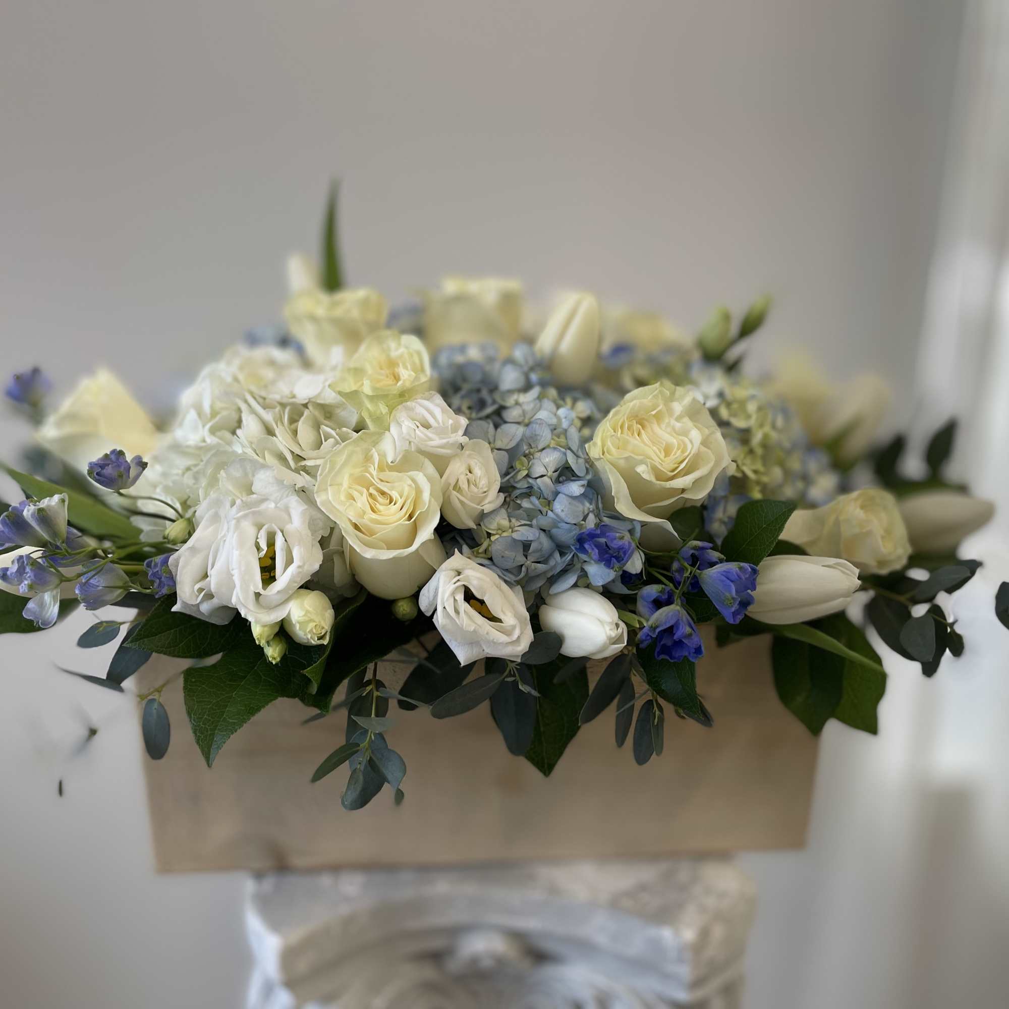 Low wooden box arrangement with white roses, tulips, lisianthus and blue hydrangeas.
