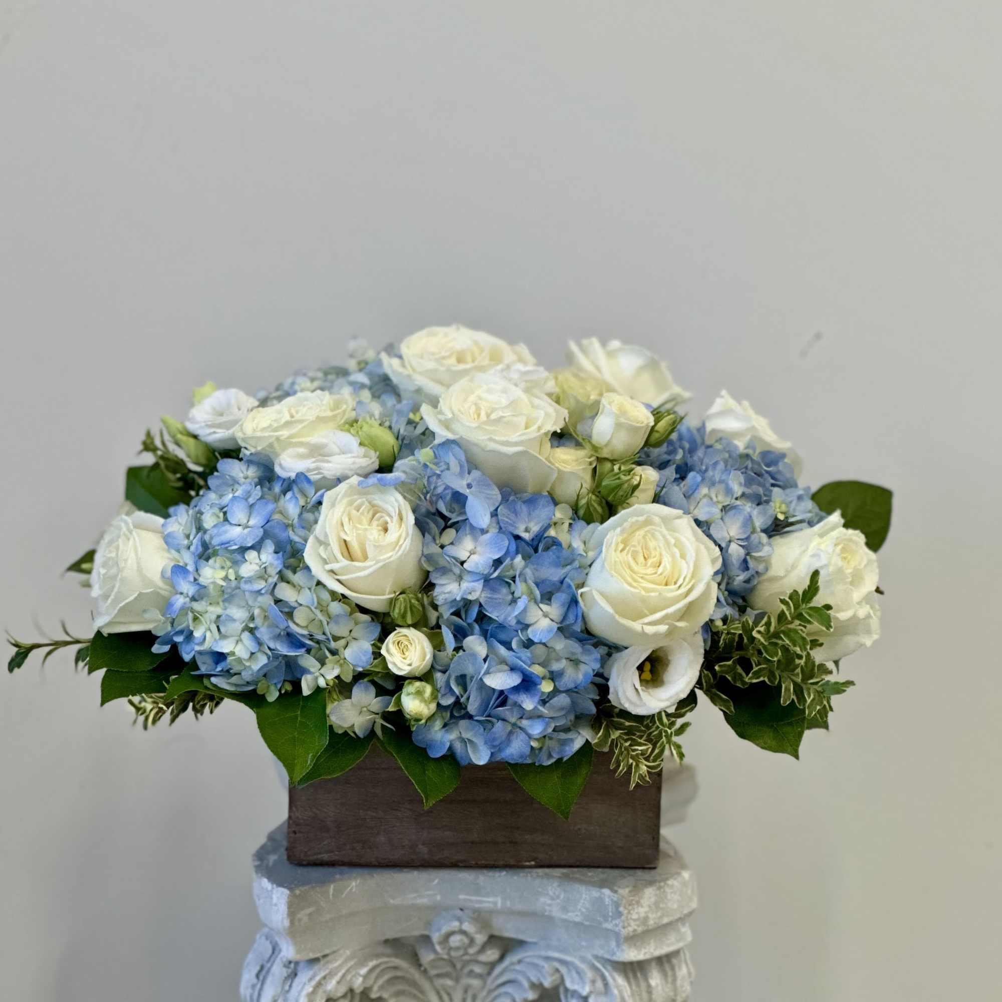 Low arrangement of white roses and blue hydrangeas in a wooden box container
