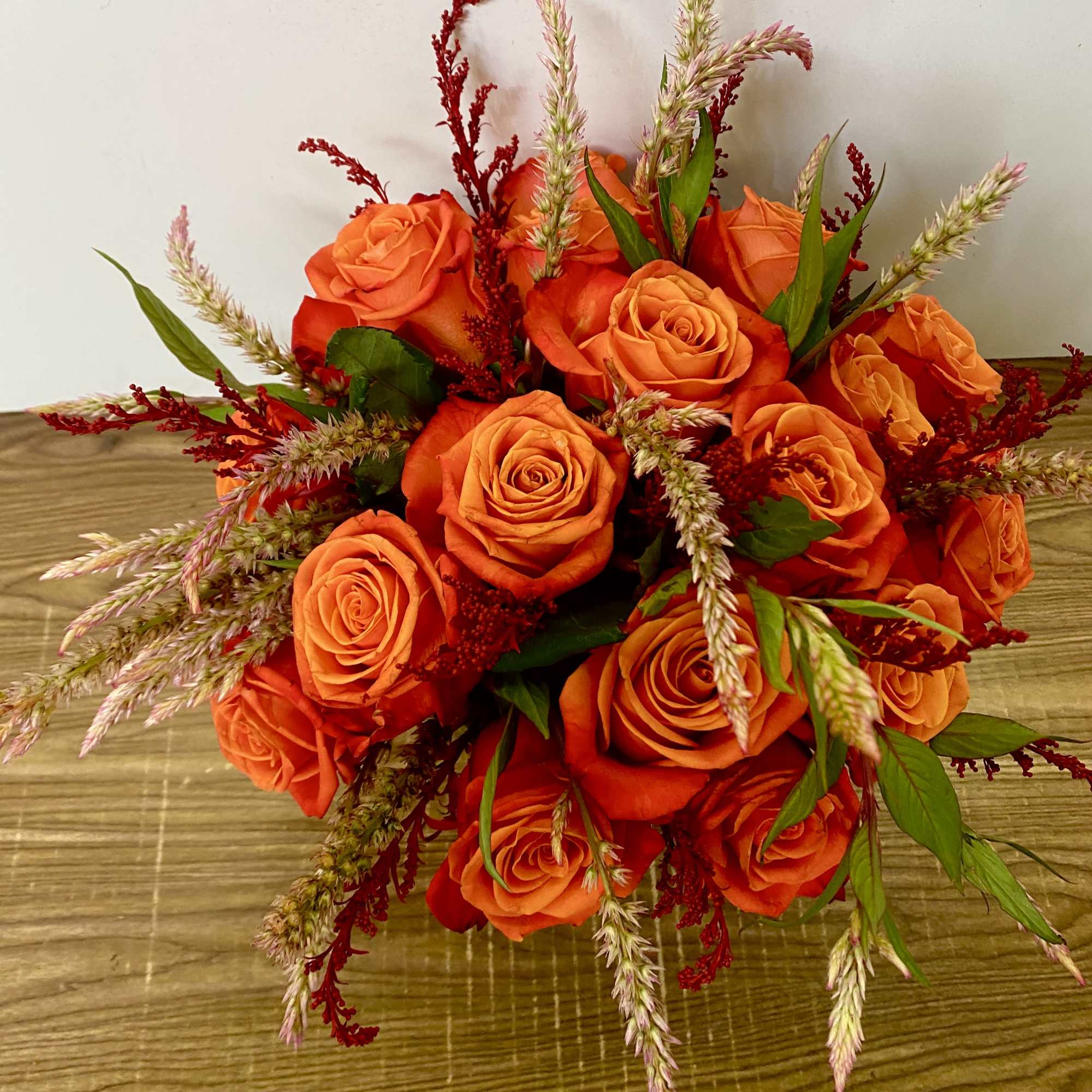 Bouquet of orange roses with red filler flowers and green accents