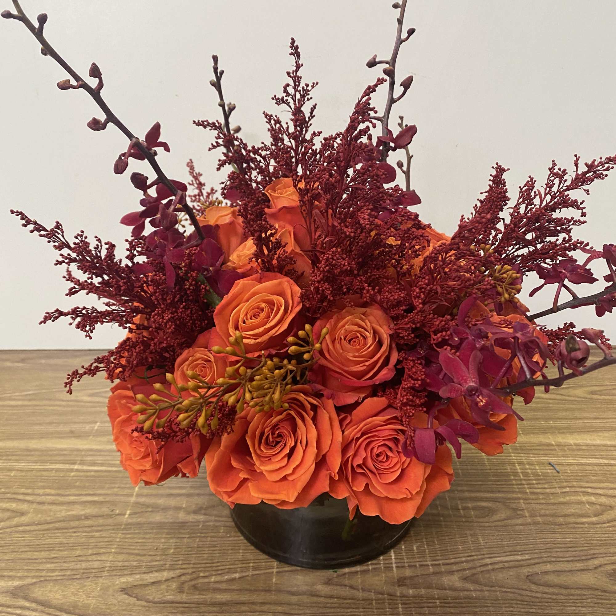 Orange roses in a black vase with burgundy branches