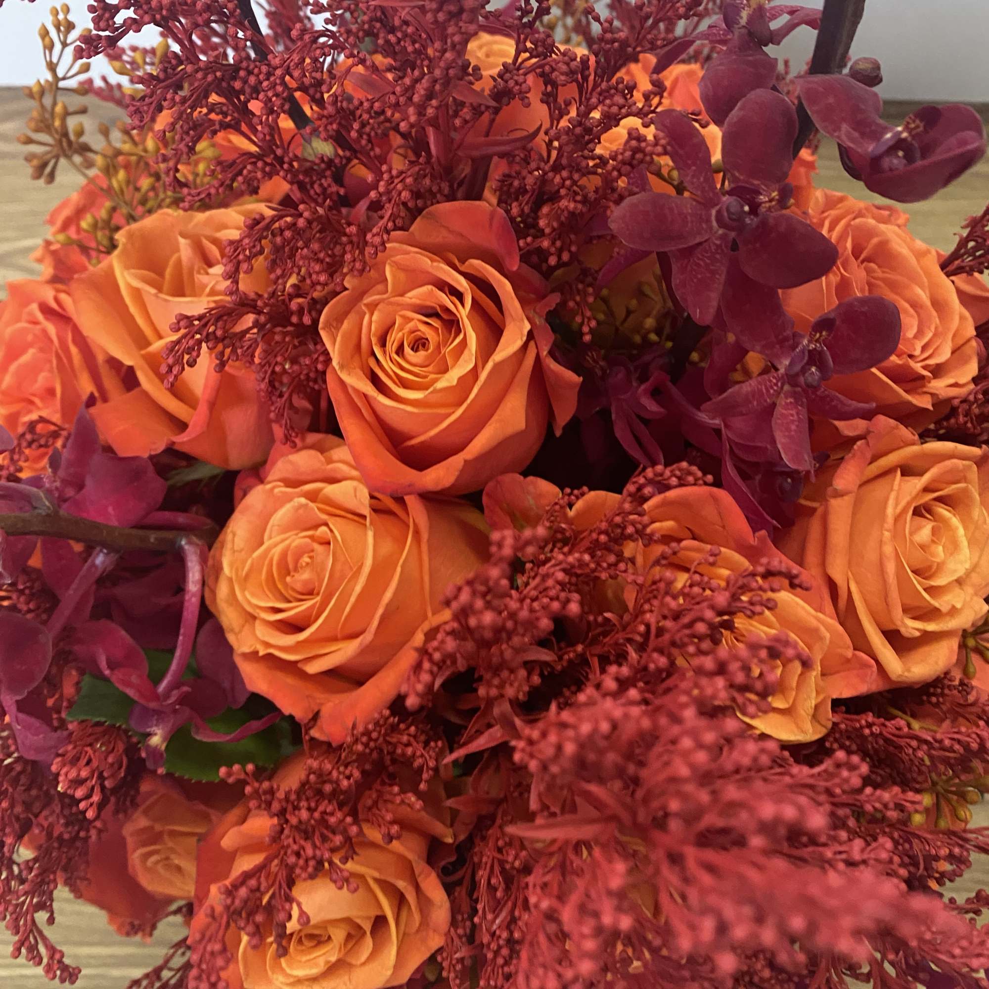 Bouquet of orange roses with burgundy orchids and filler flowers