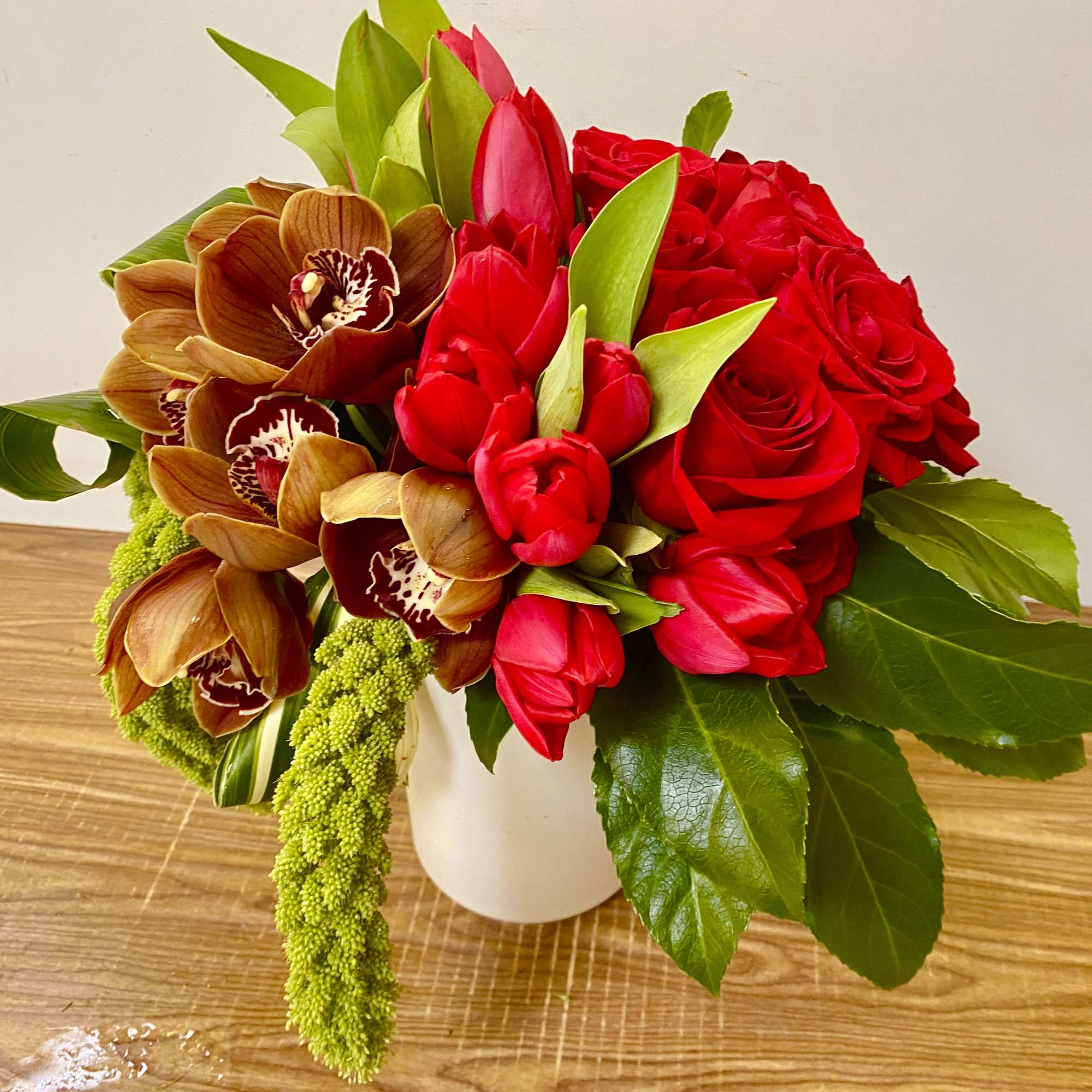 Bouquet of red roses, red tulips, and brown orchids in a white vase