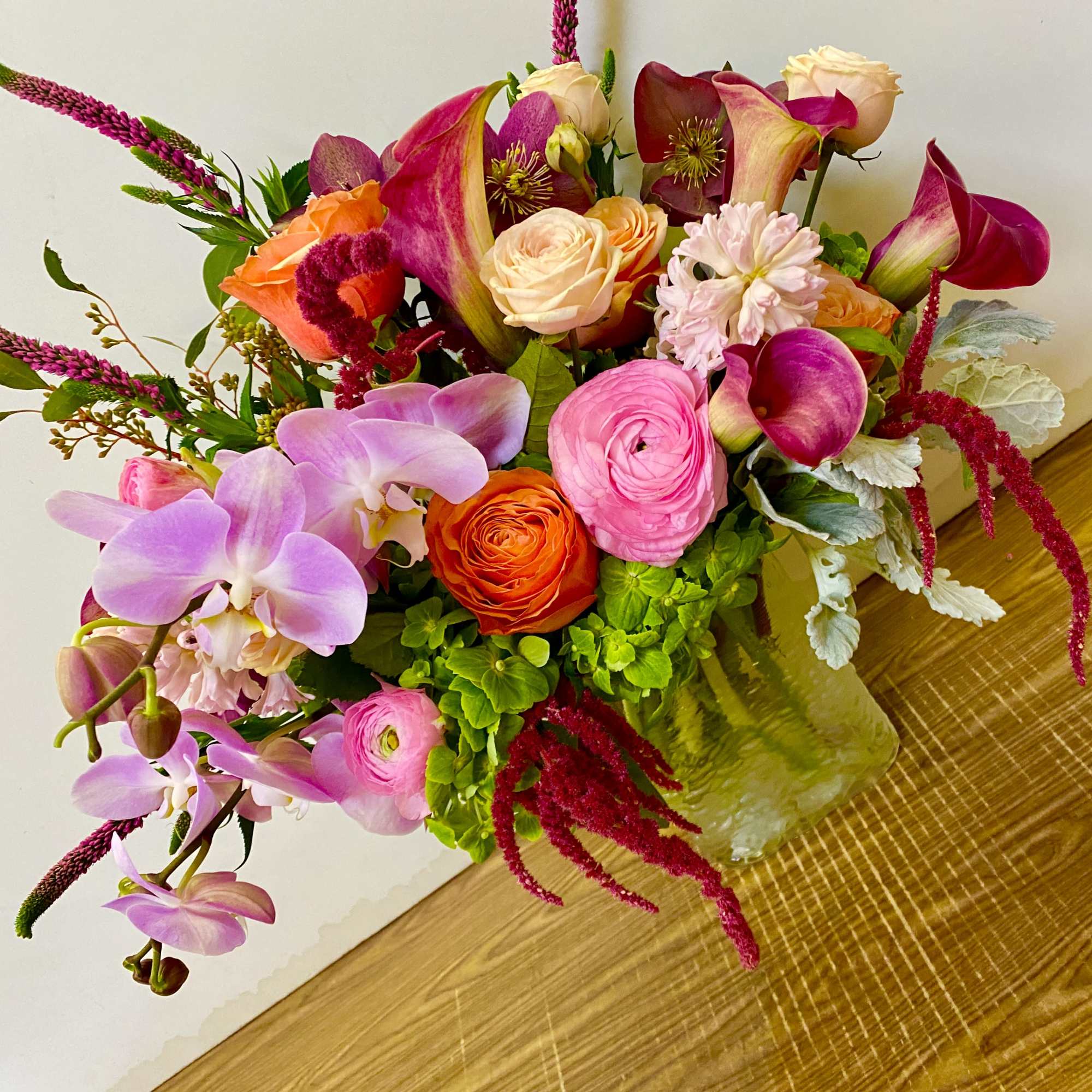 Colorful bouquet with orchids, roses, calla lilies, and pink accents in a glass vase