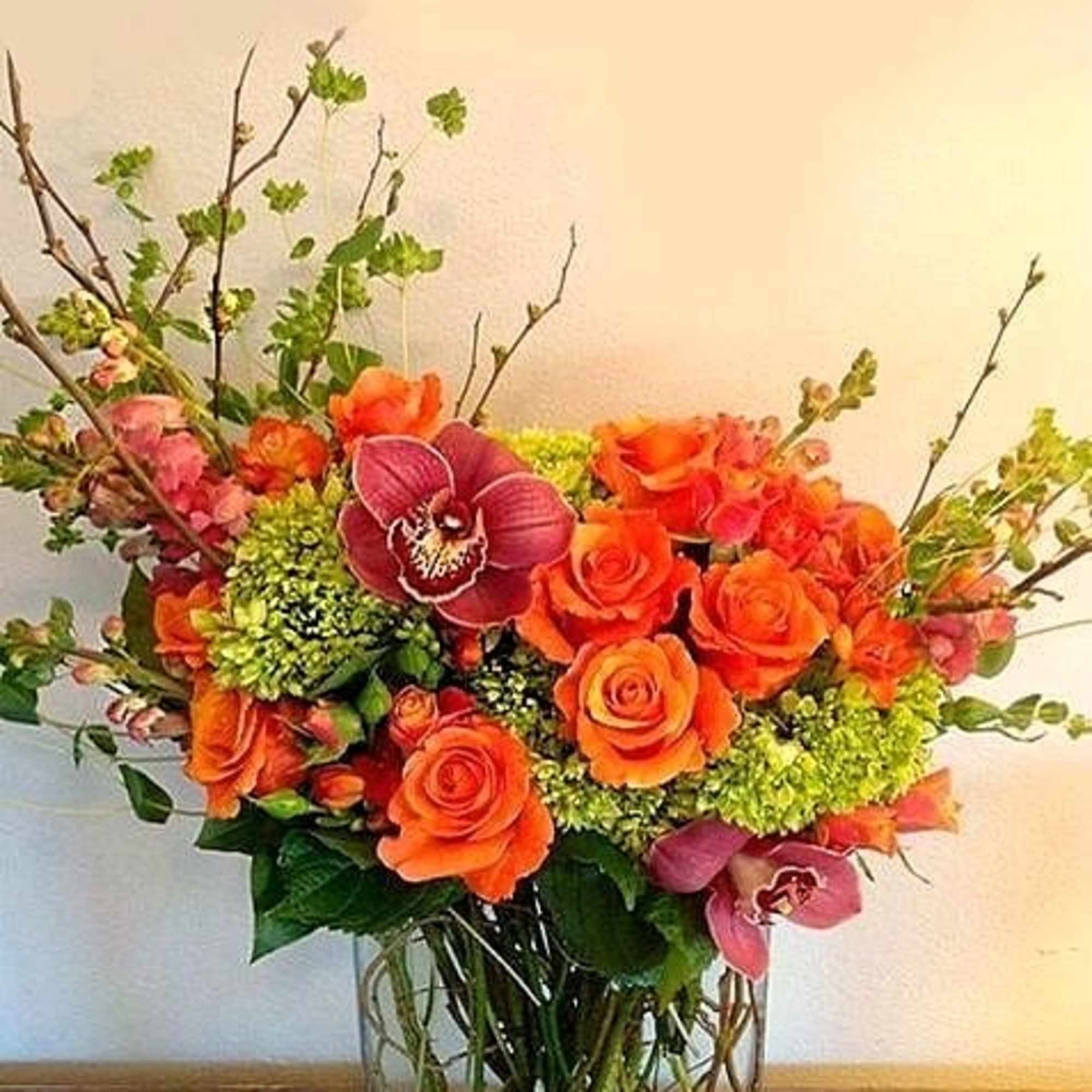 Orange roses and pink orchids arranged in a clear glass vase