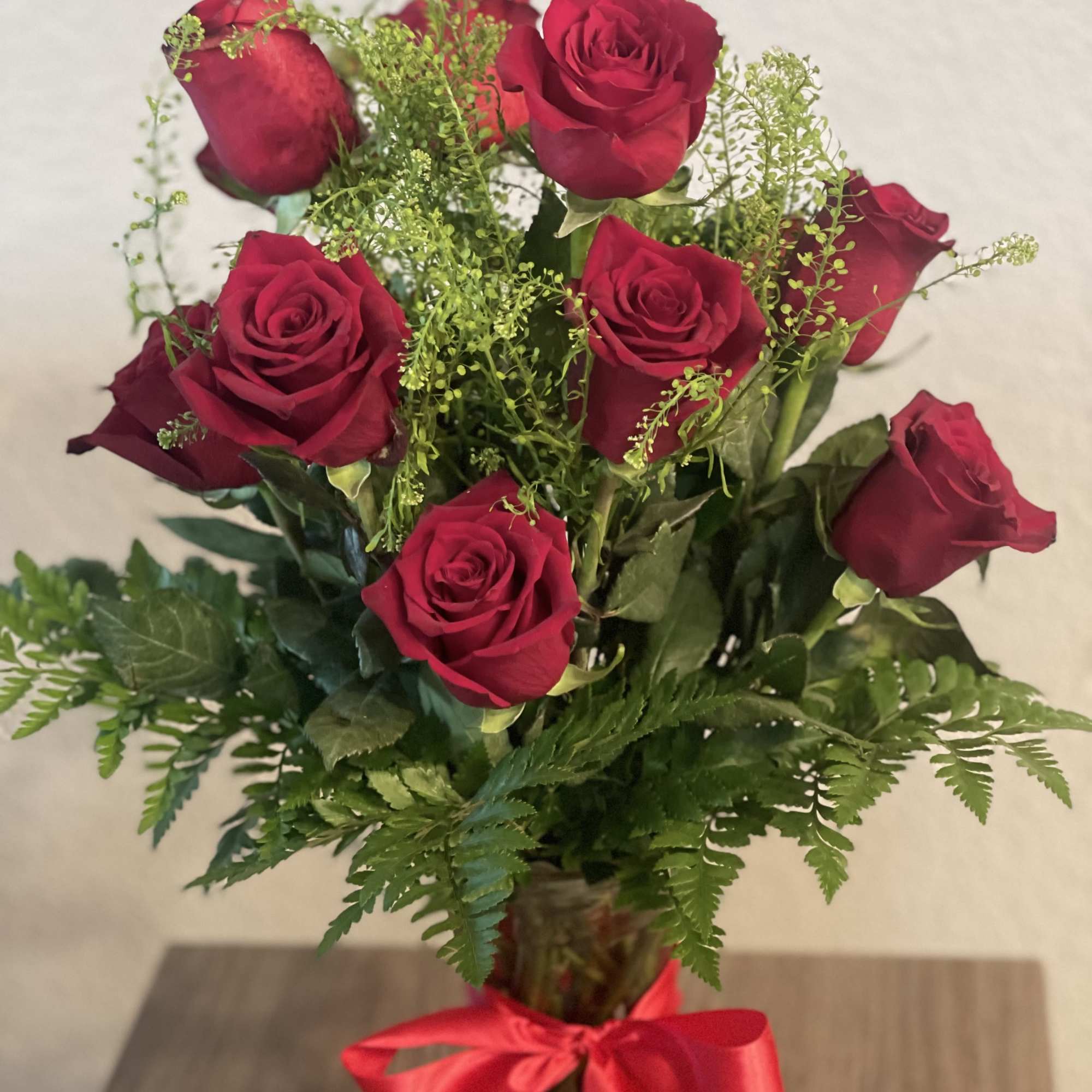 Bouquet of red roses with fern foliage in a glass vase tied with a red ribbon