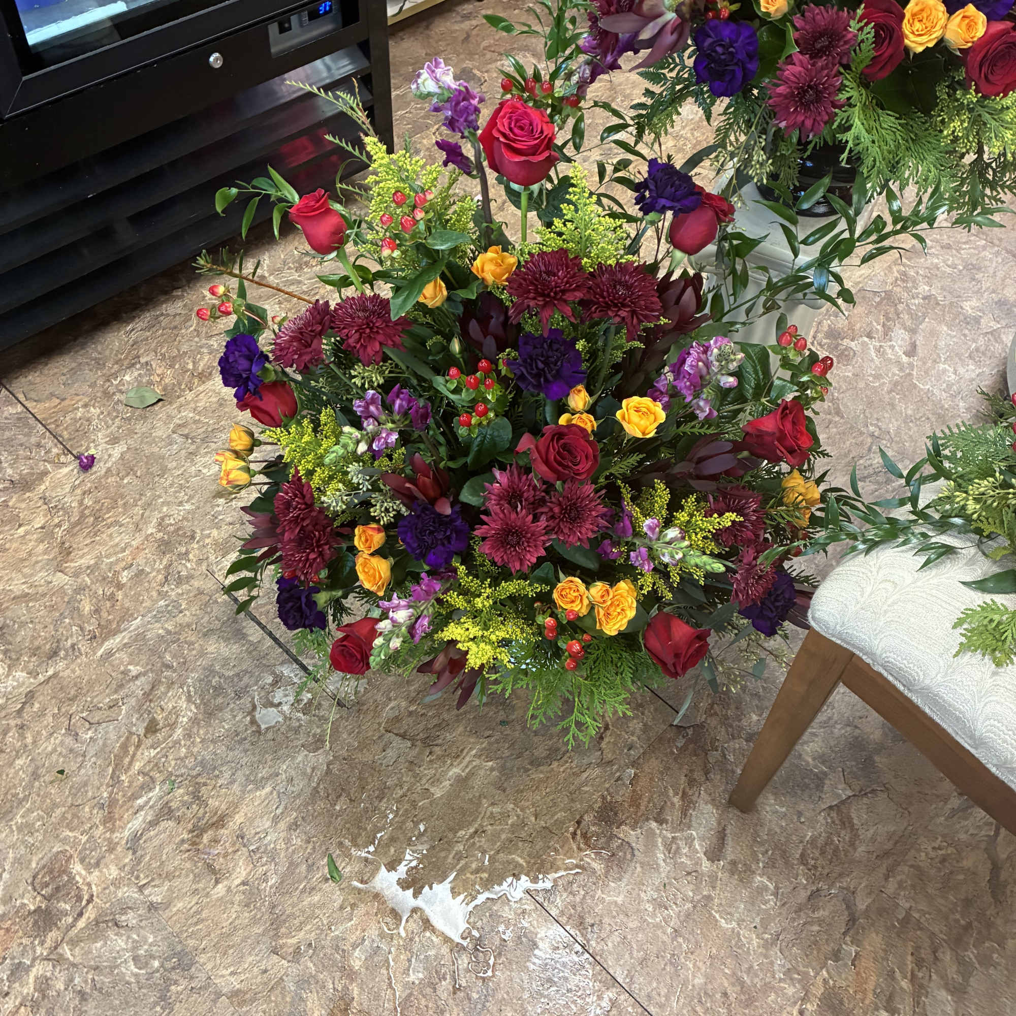 Large mixed floral arrangement with red roses, purple blooms, and yellow spray roses