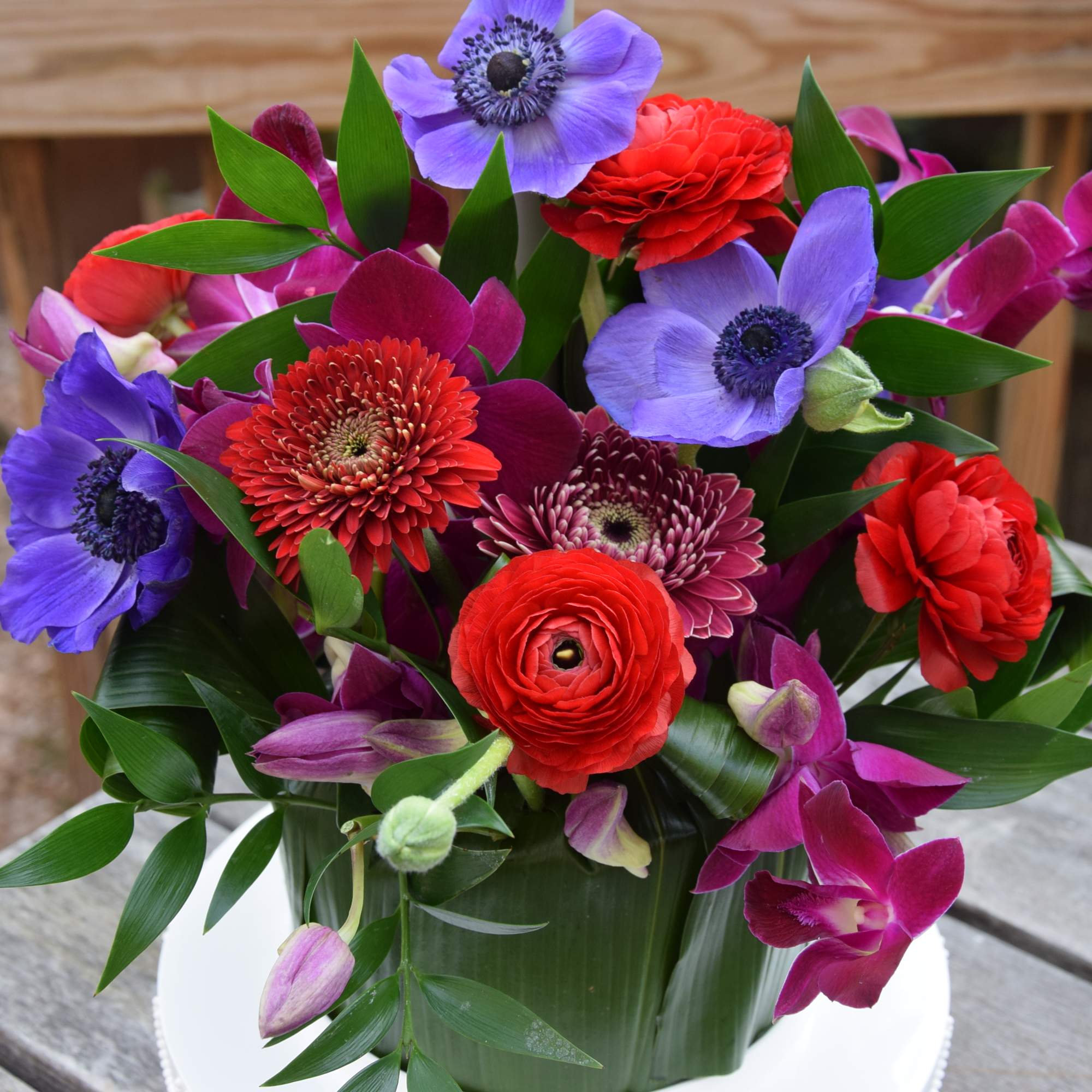 Bright mixed bouquet with purple, red, and magenta flowers in a white container