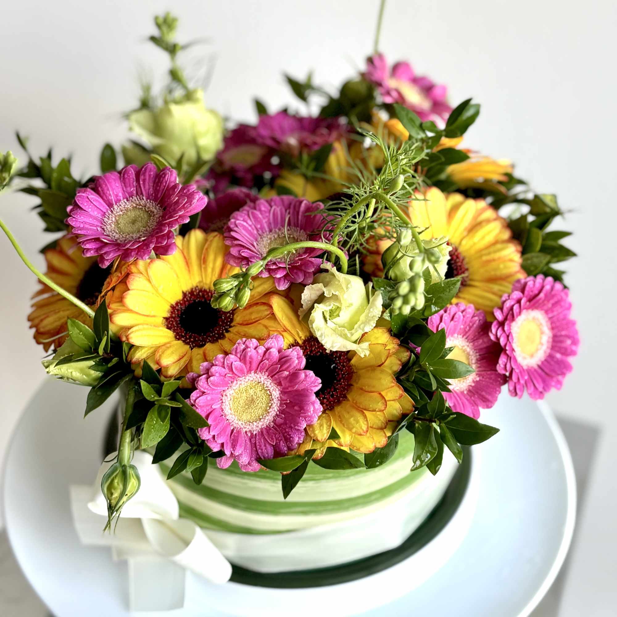 Bright gerbera daisy arrangement in a striped round box with a white ribbon