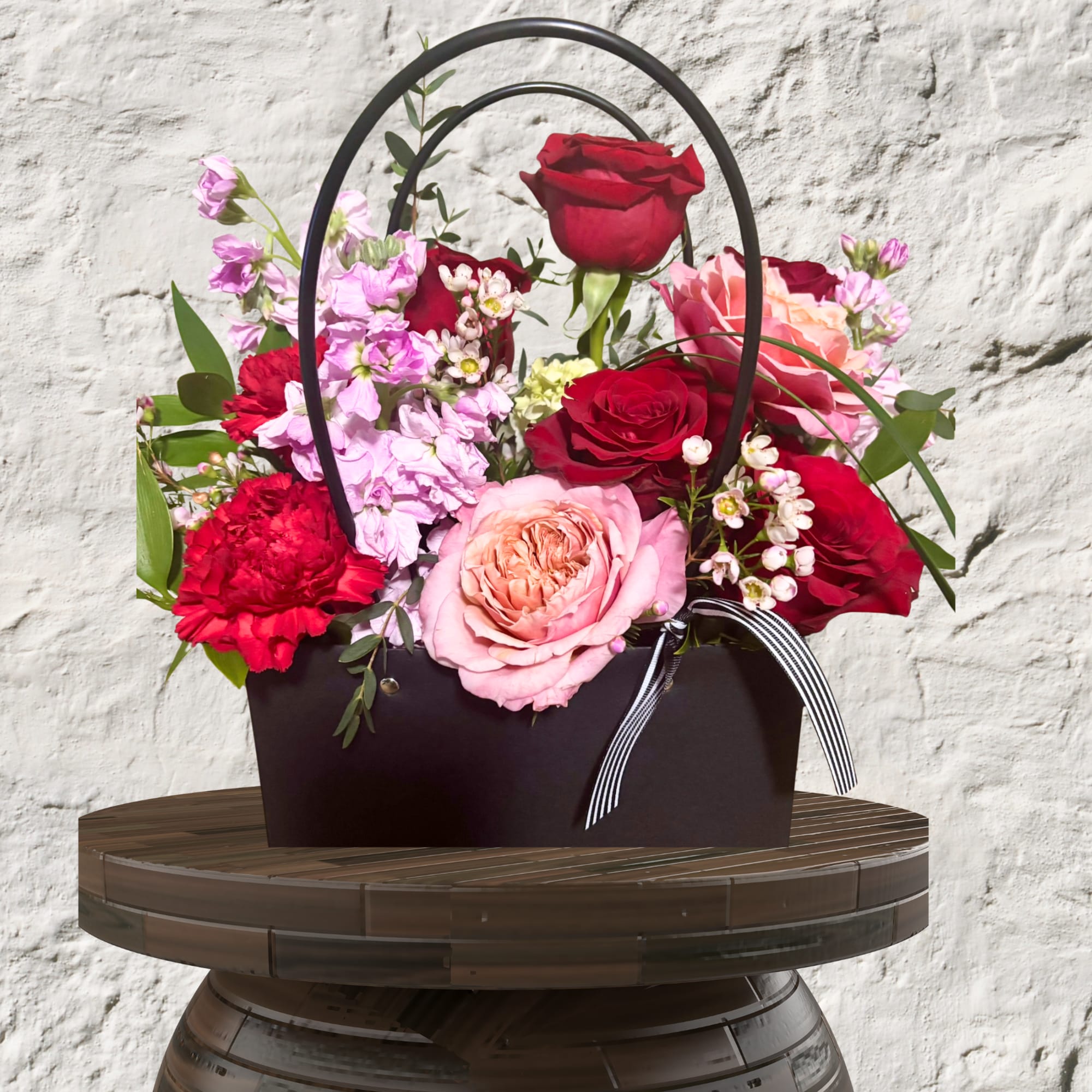 Basket arrangement of red, pink, and lavender roses with carnations