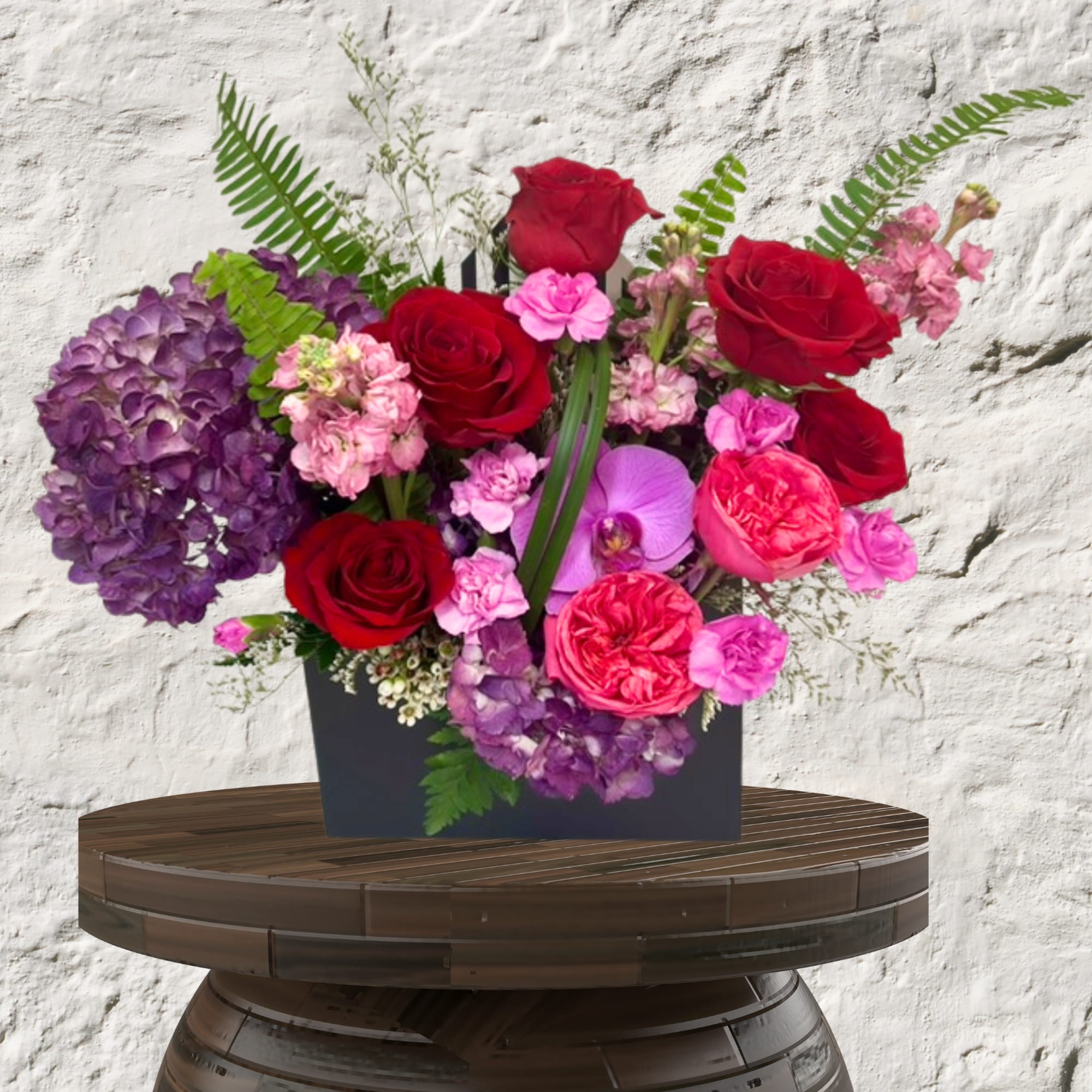 Arrangement of red roses, purple hydrangea, and pink orchids in a black box