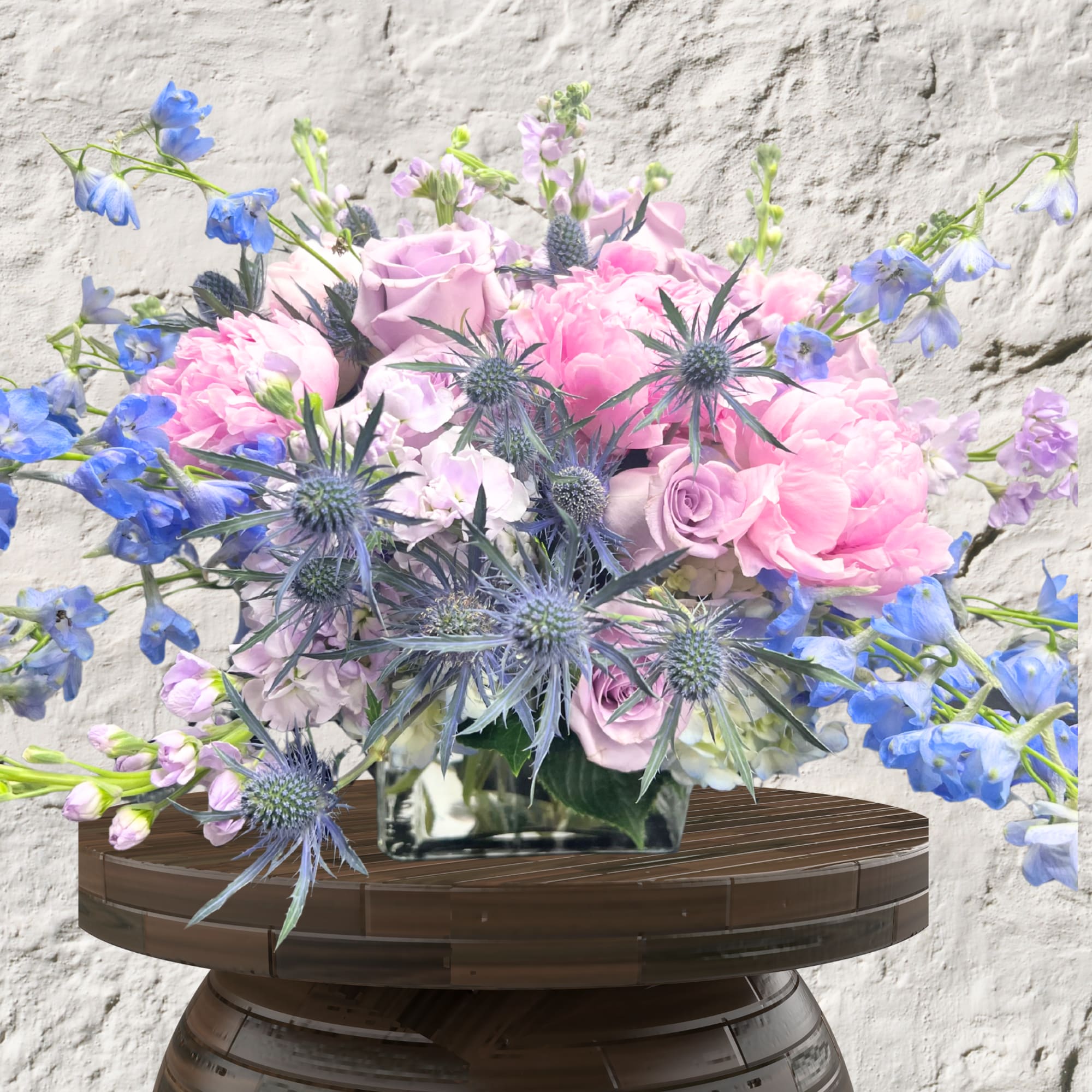 Pink roses and peonies with blue spiky thistles in a glass vase