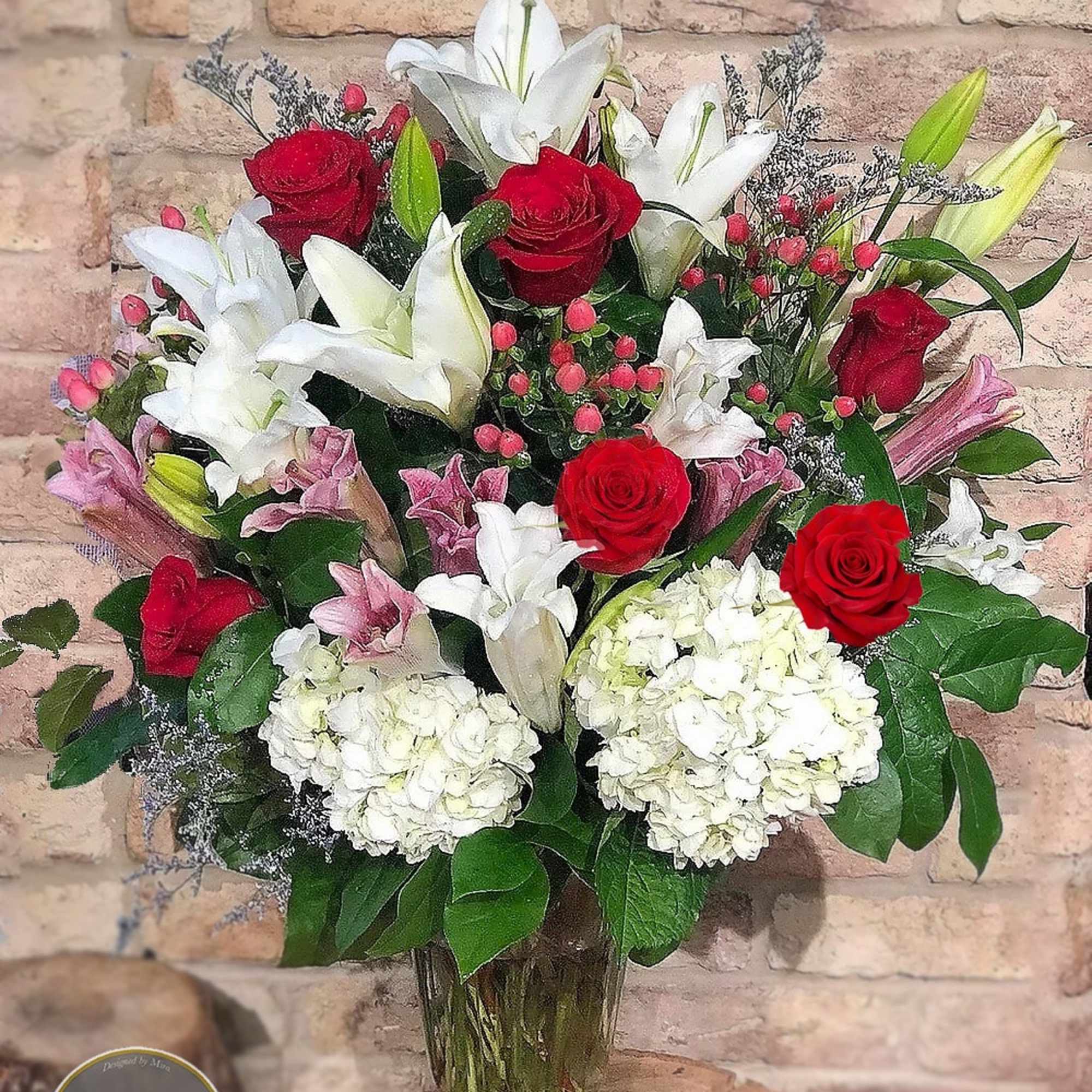 Tall bouquet of red roses, white and pink lilies, and white hydrangeas in a clear glass vase