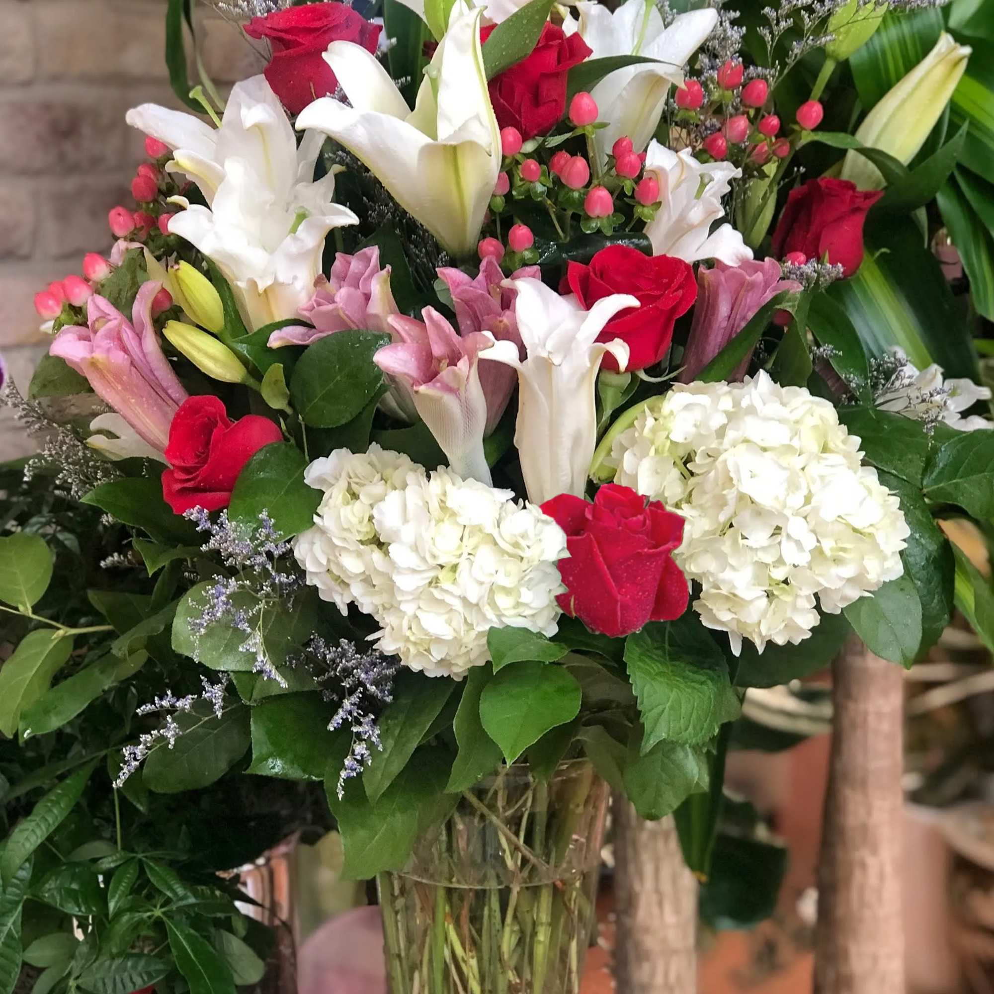Tall glass vase of white lilies, hydrangeas, and red roses with pink accents in a lush arrangement