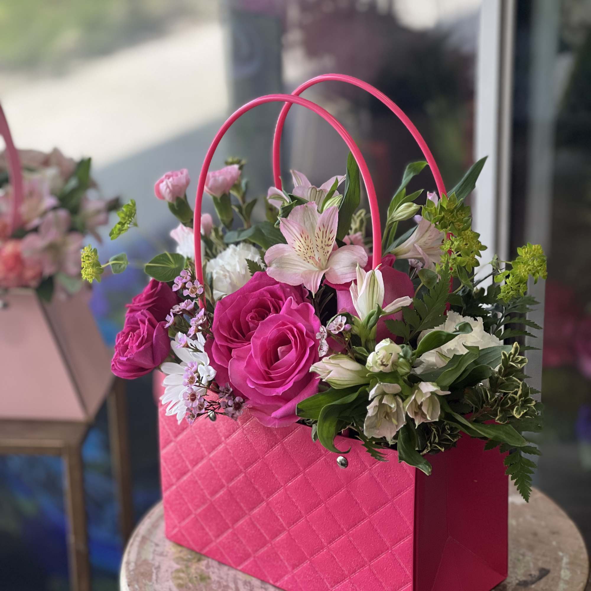 Pink floral arrangement in a quilted handbag-style box with arched handles