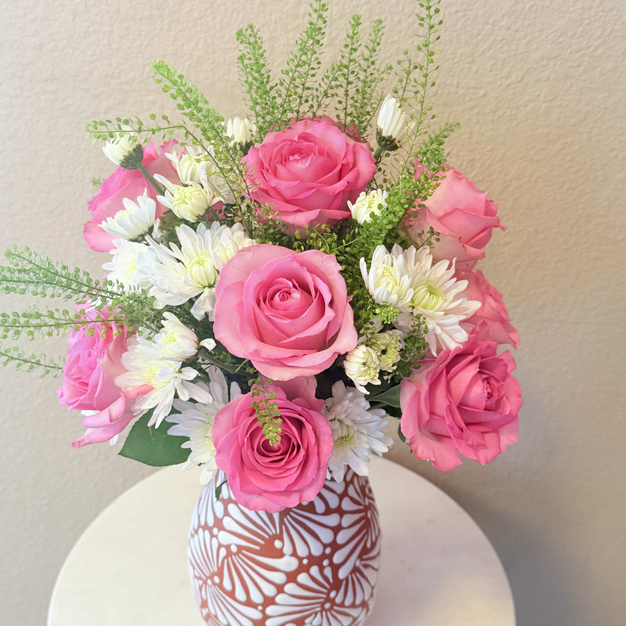 Bright pink roses mingle with cheerful white daisy-like blooms and airy green