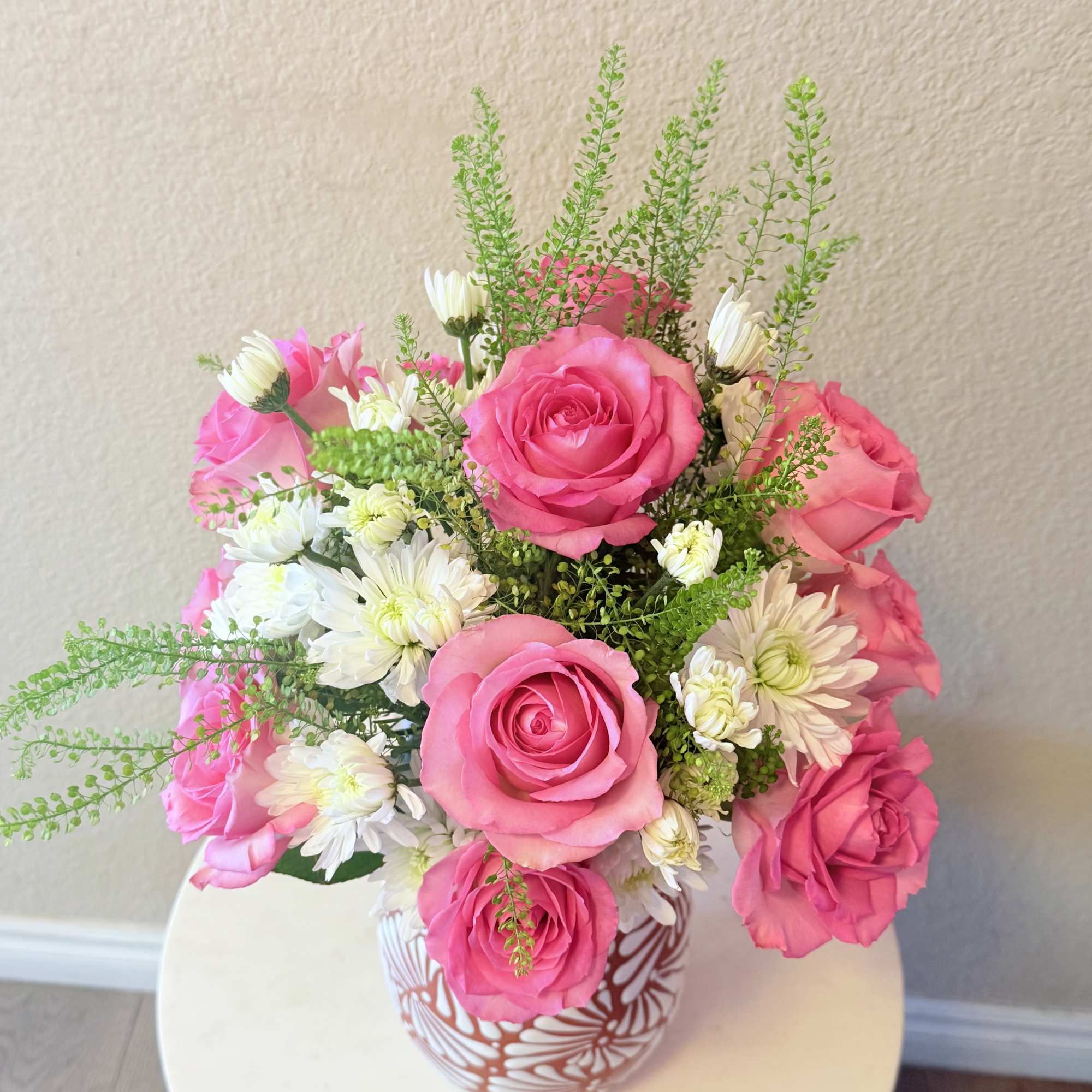 Bright pink roses mingle with cheerful white daisy-like blooms and airy green