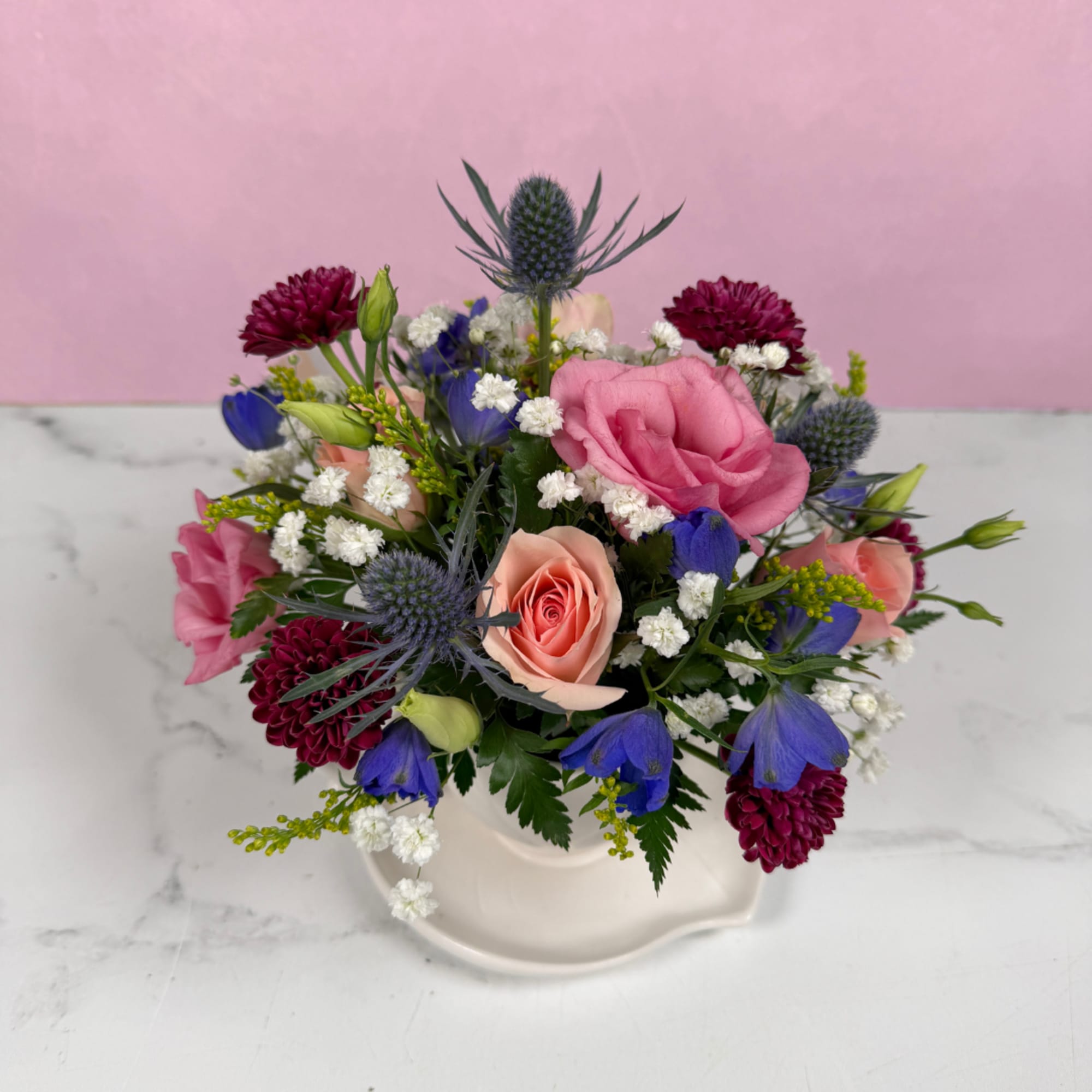 Soft blush roses and lively blue blooms spill from a white teacup