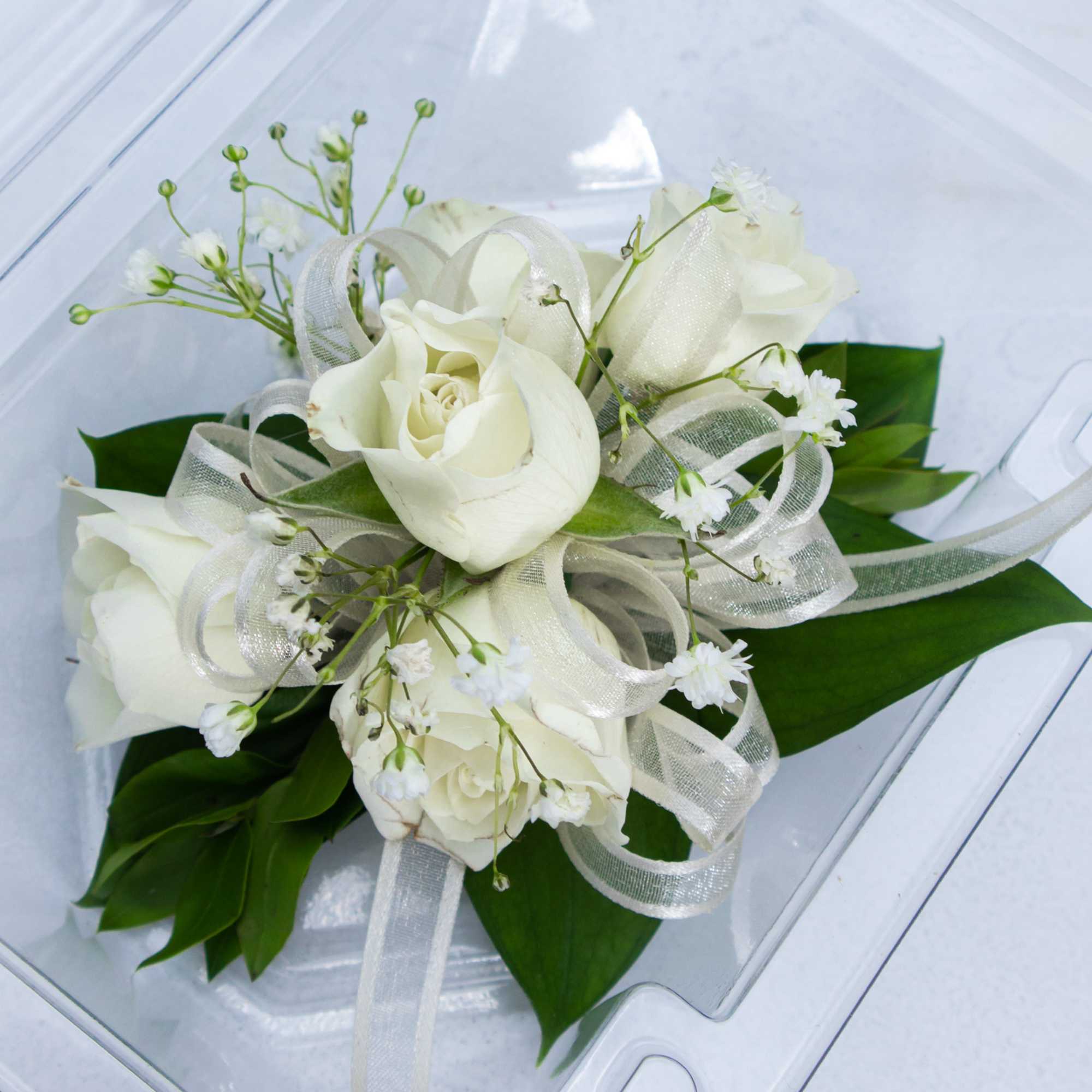 White rose bouquet with ribbon and green leaves in a clear box