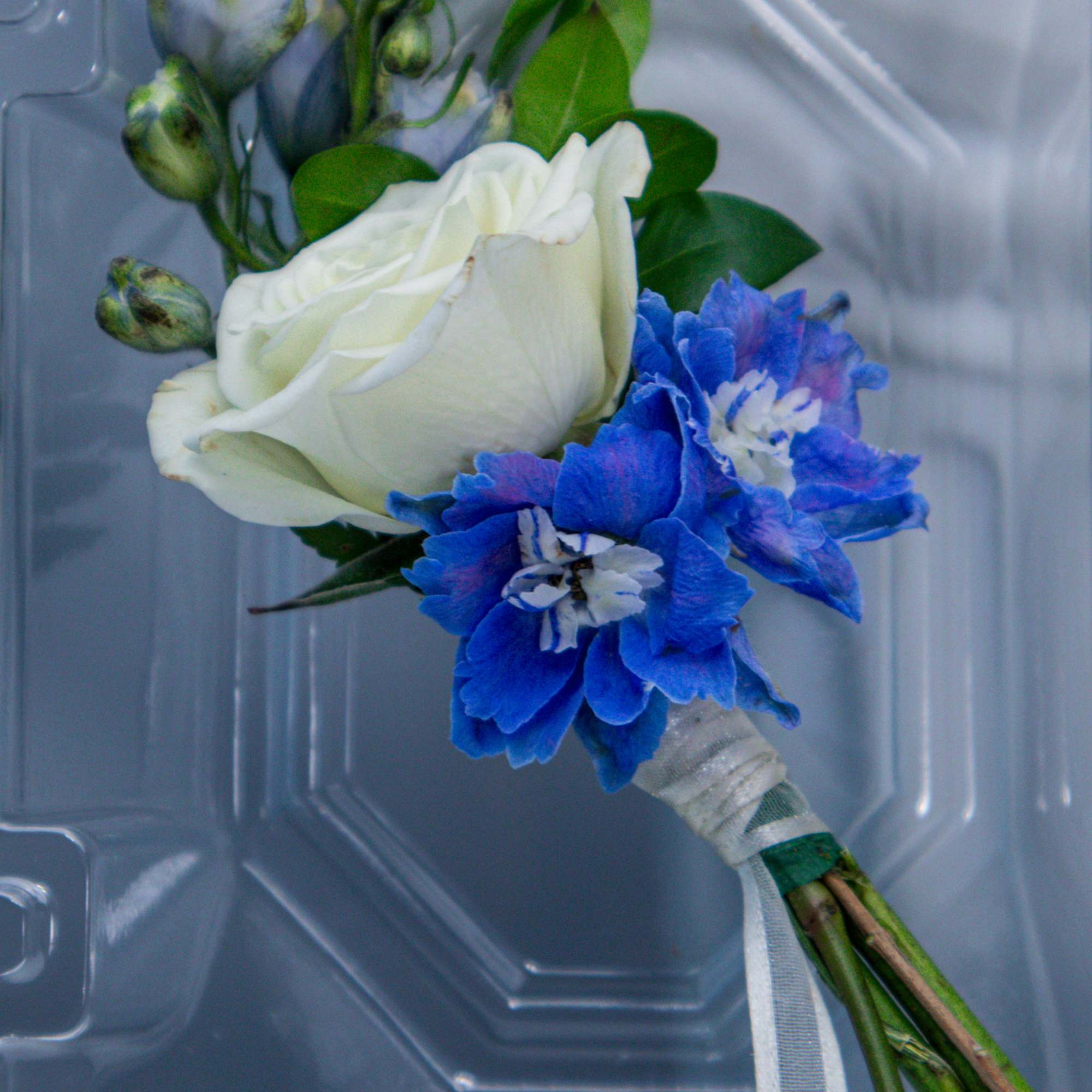 White rose boutonniere with blue flowers and ribbon wrap