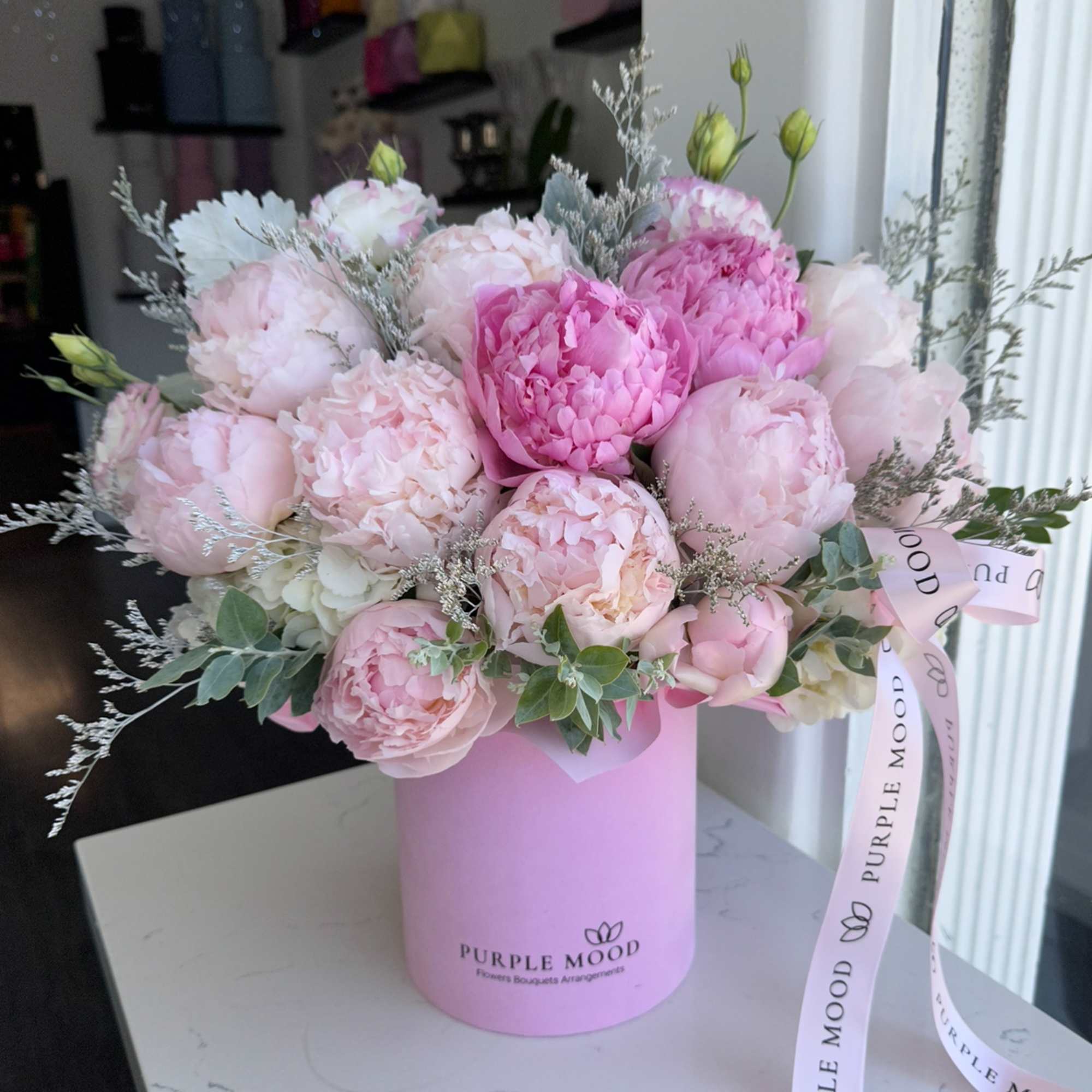 Pink peonies and roses arranged in a pink hat box with ribbon