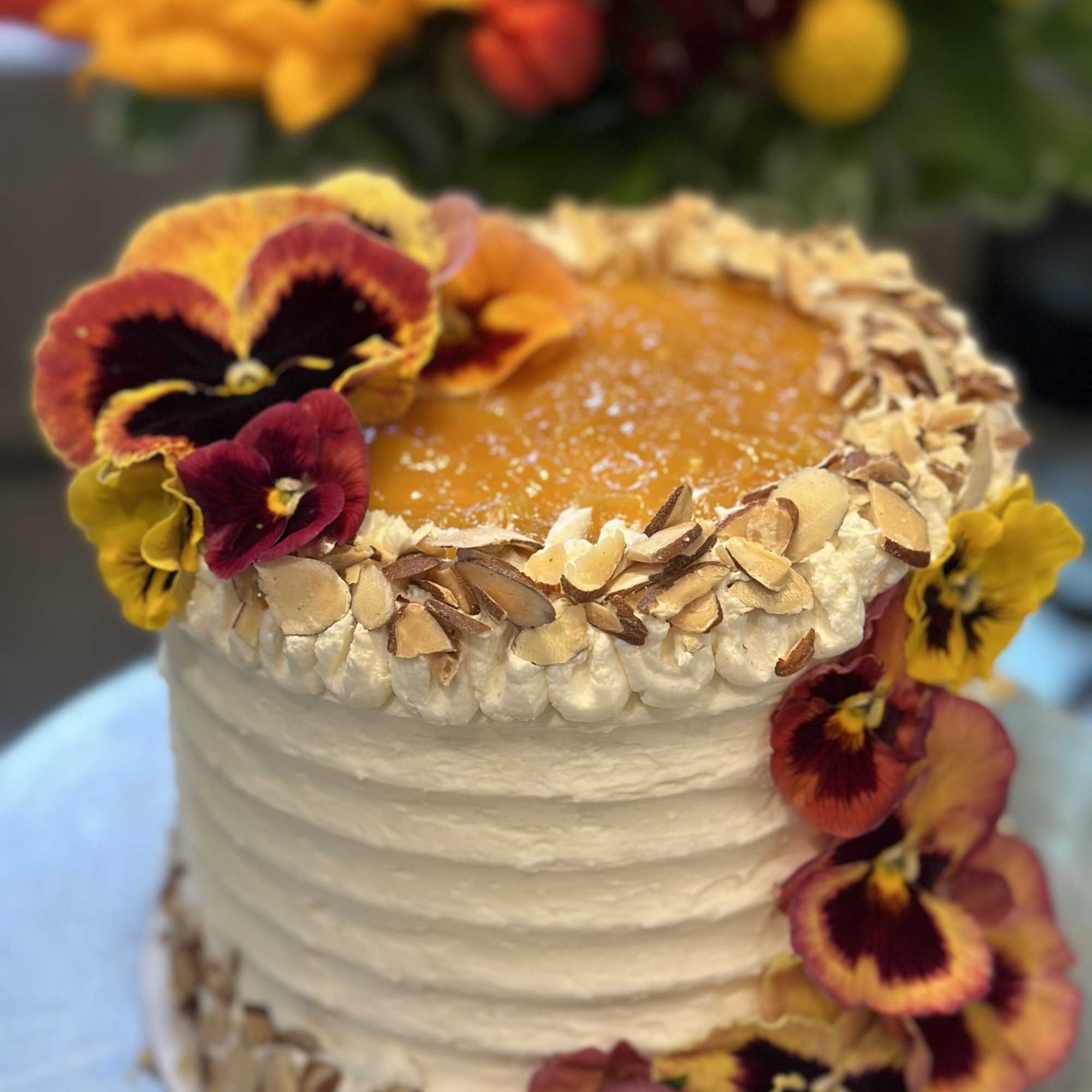 White frosted cake decorated with pansies and almond slices